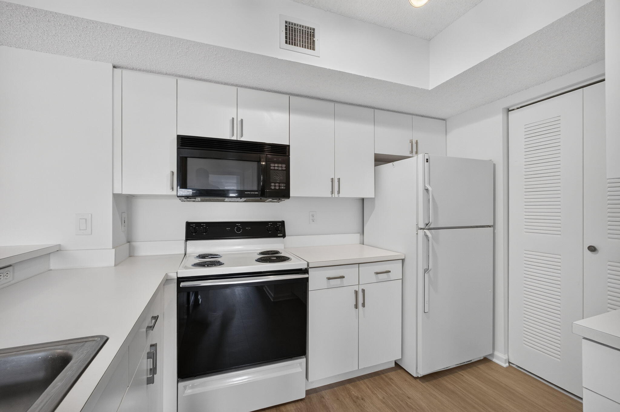 Kitchen featuring white cabinetry, solid-surface countertops, vinyl plank flooring, and built-in appliances including a microwave, range, and refrigerator.