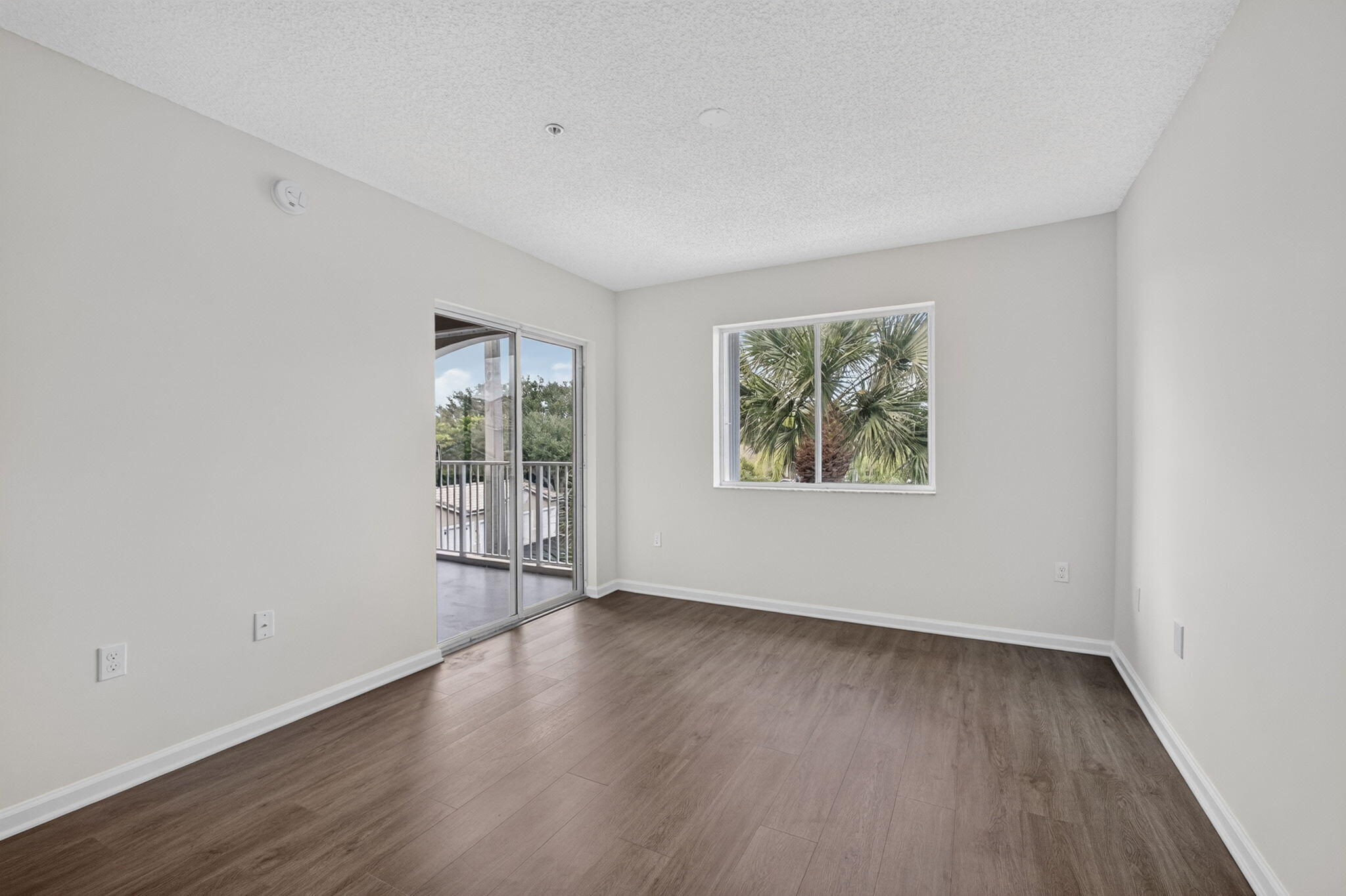 Neutral-toned interior featuring vinyl plank flooring, sliding glass door, leading to balcony and a horizontal window