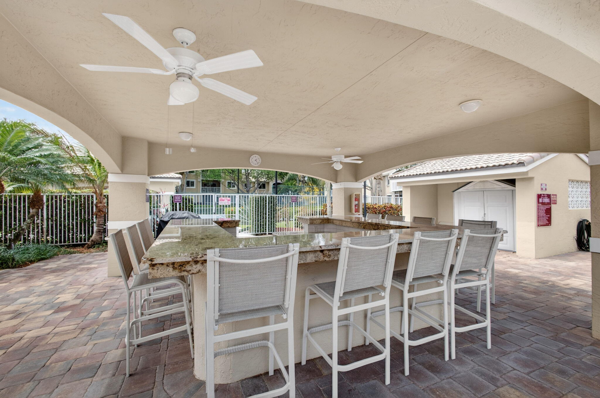 Covered outdoor bar area featuring a stone-topped bar, paver patio flooring, and overhead ceiling fans