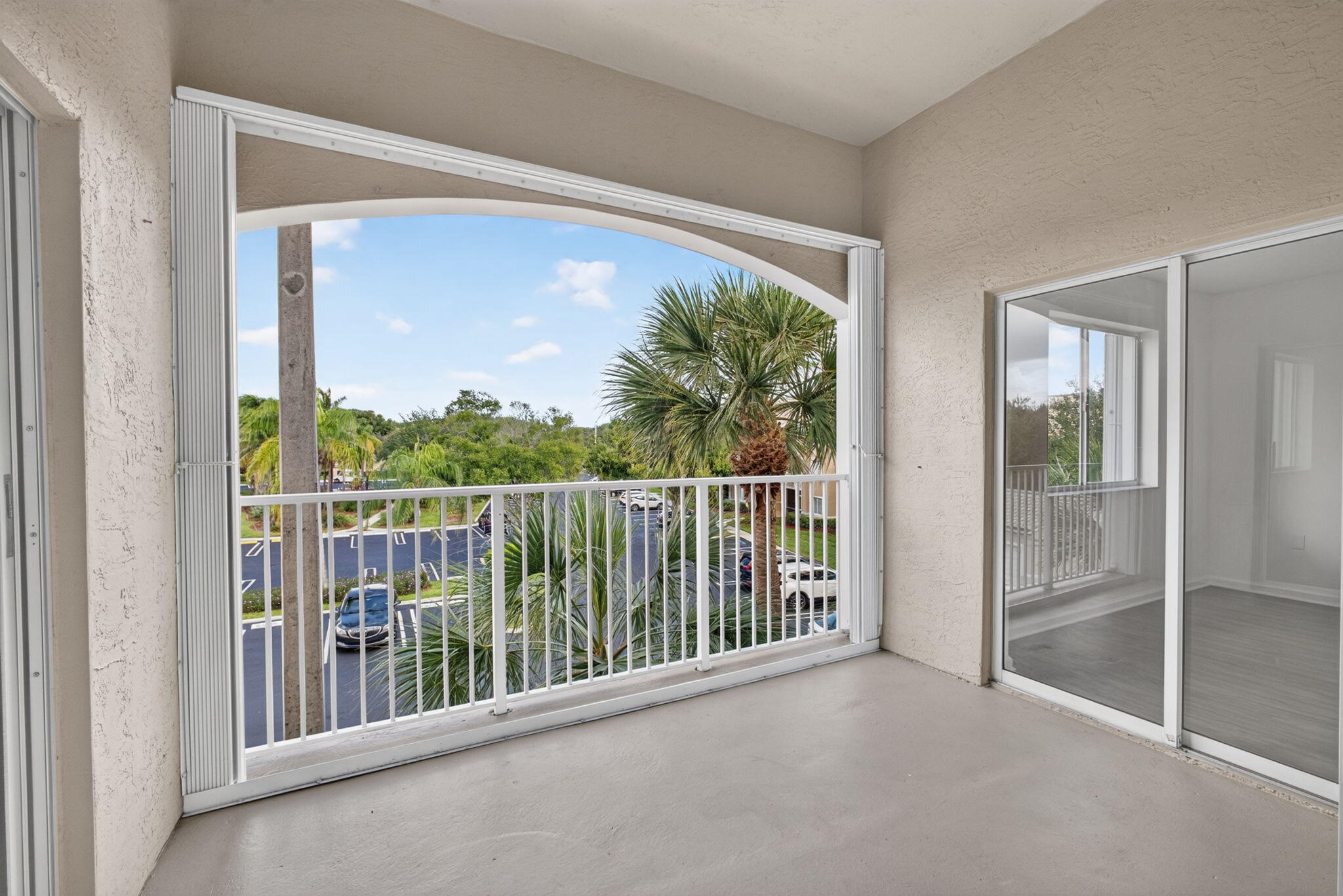 Covered balcony featuring a white metal railing, arched architectural detailing, and sliding glass door access to living area and bedrooms.