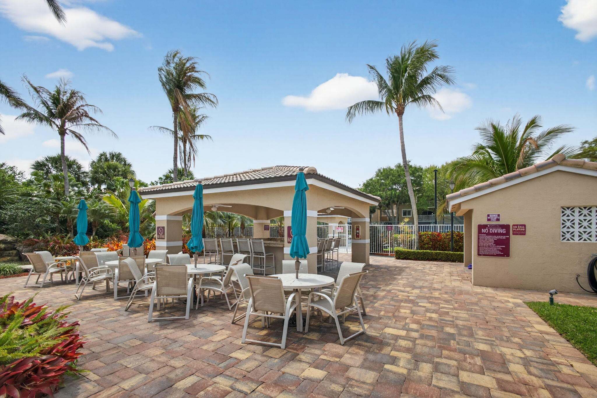 Covered outdoor pavilion featuring a built-in stone bar and tiled roofing, set within a landscaped patio finished with decorative pavers