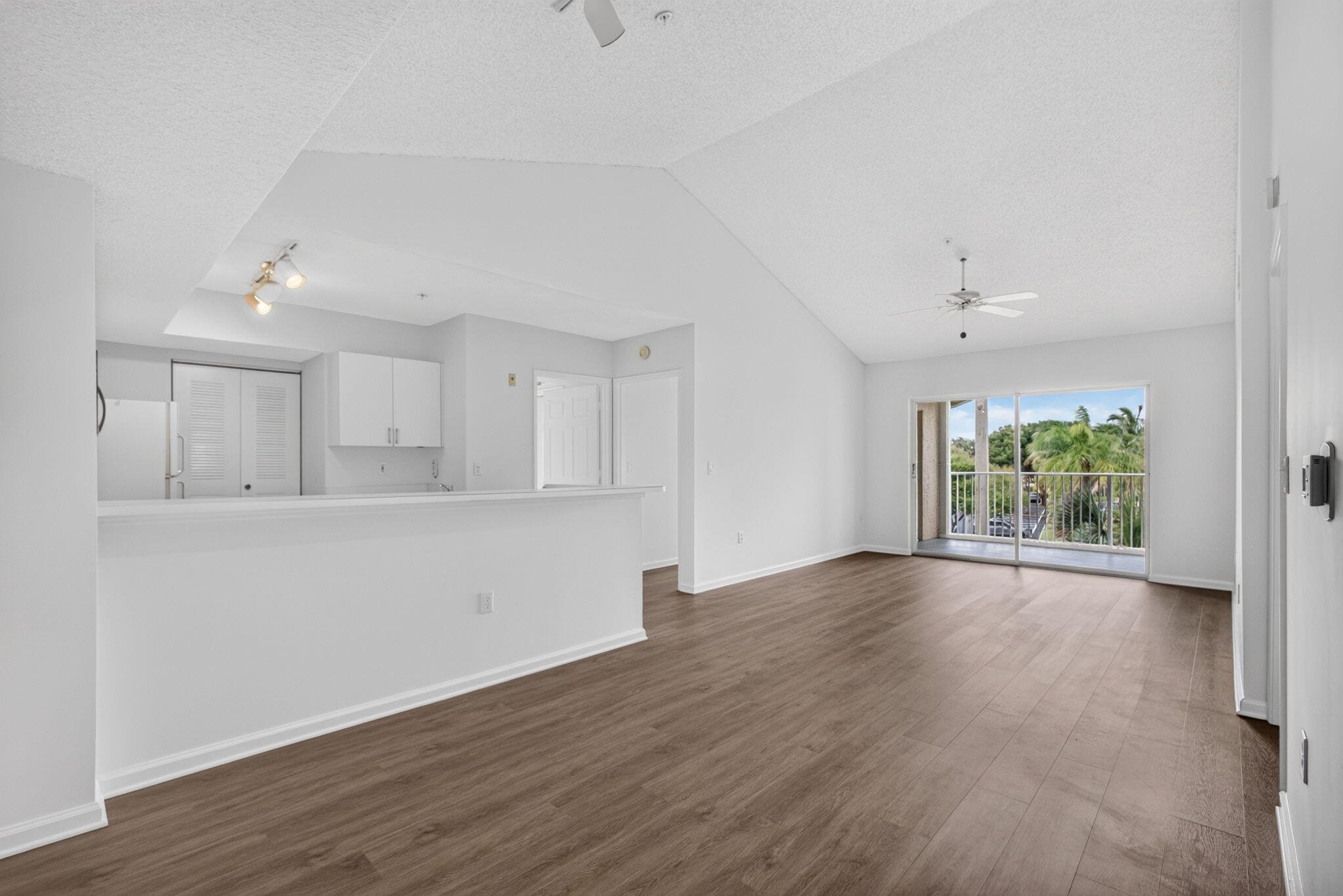 Open-concept interior featuring vaulted ceilings, vinyl plank flooring, a breakfast bar, recessed lighting and sliding glass doors leading to balcony.