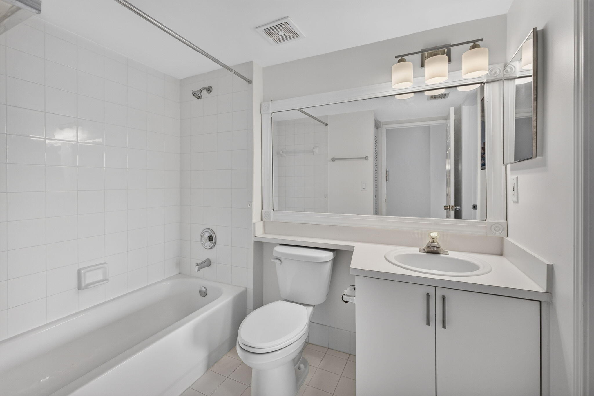 Bathroom featuring a tub-shower combination with floor-to-ceiling tile surround, white cabinetry, integrated sink with countertop, oversized wall-mounted mirror, and three-light fixture