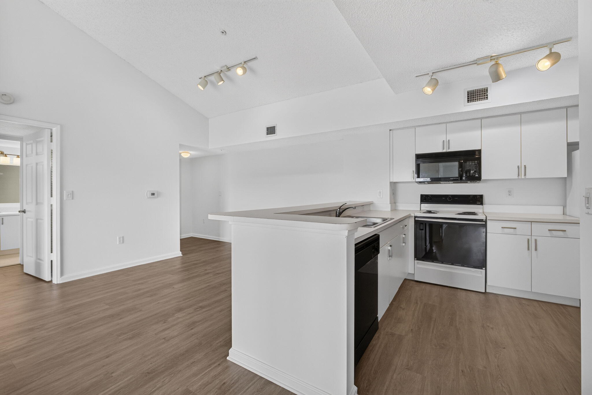 Kitchen featuring white cabinetry, vinyl plank flooring, vaulted ceilings, track lighting, and a breakfast bar.