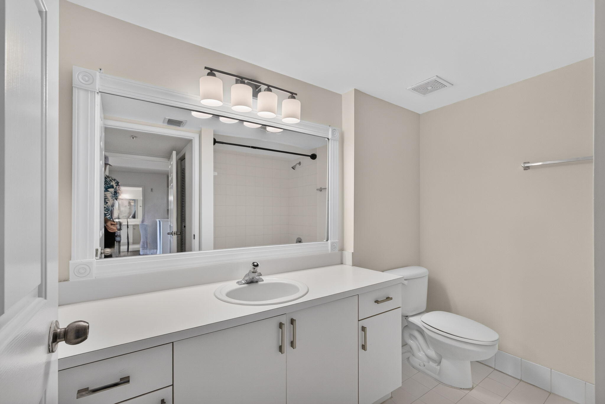 Bathroom featuring a white vanity cabinet with countertop basin, large framed wall mirror, four-light vanity fixture, and tiled flooring