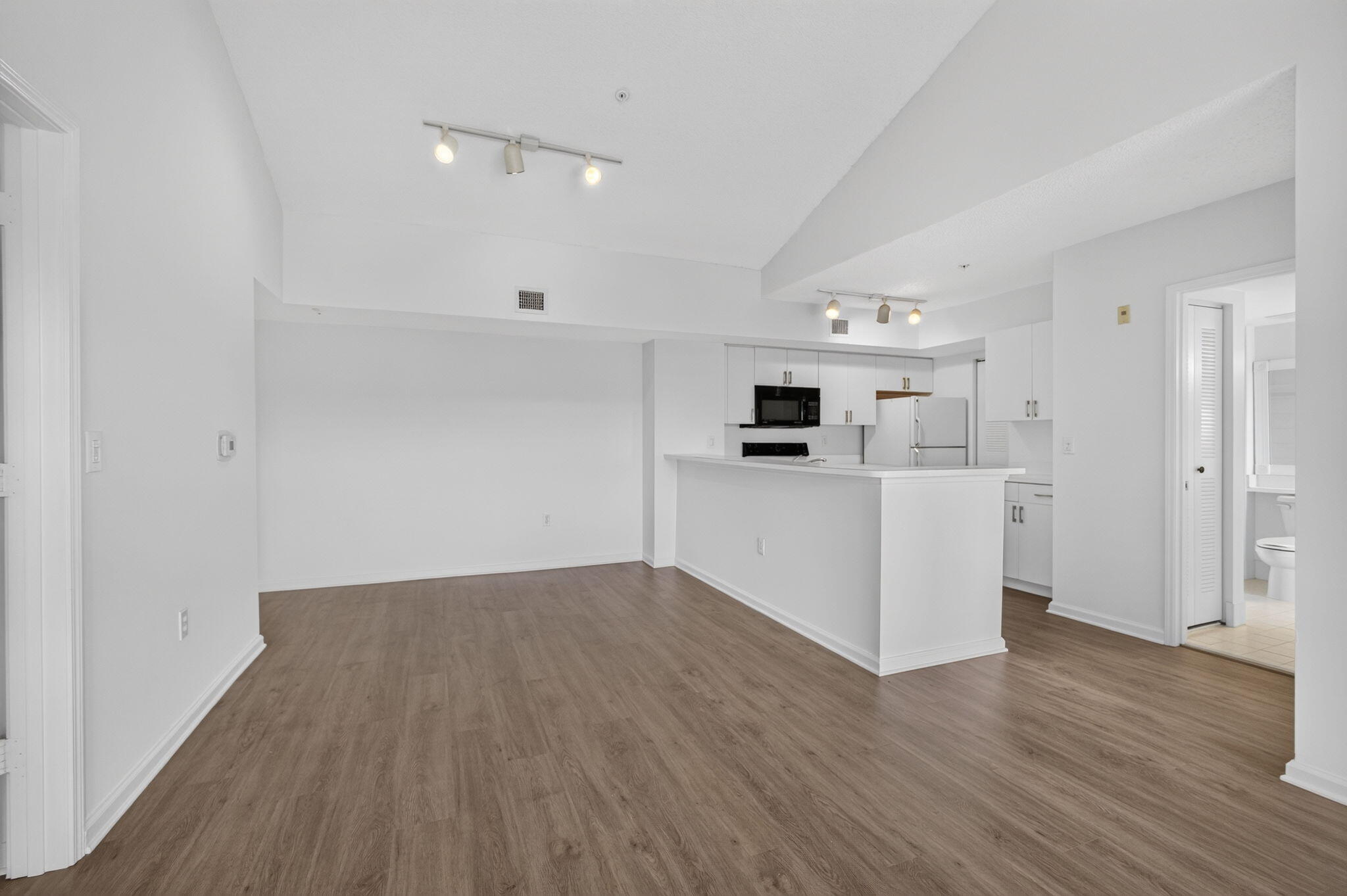 Open-concept interior featuring vaulted ceilings, vinyl plank flooring, white cabinetry, a breakfast bar, and adjustable track lighting.