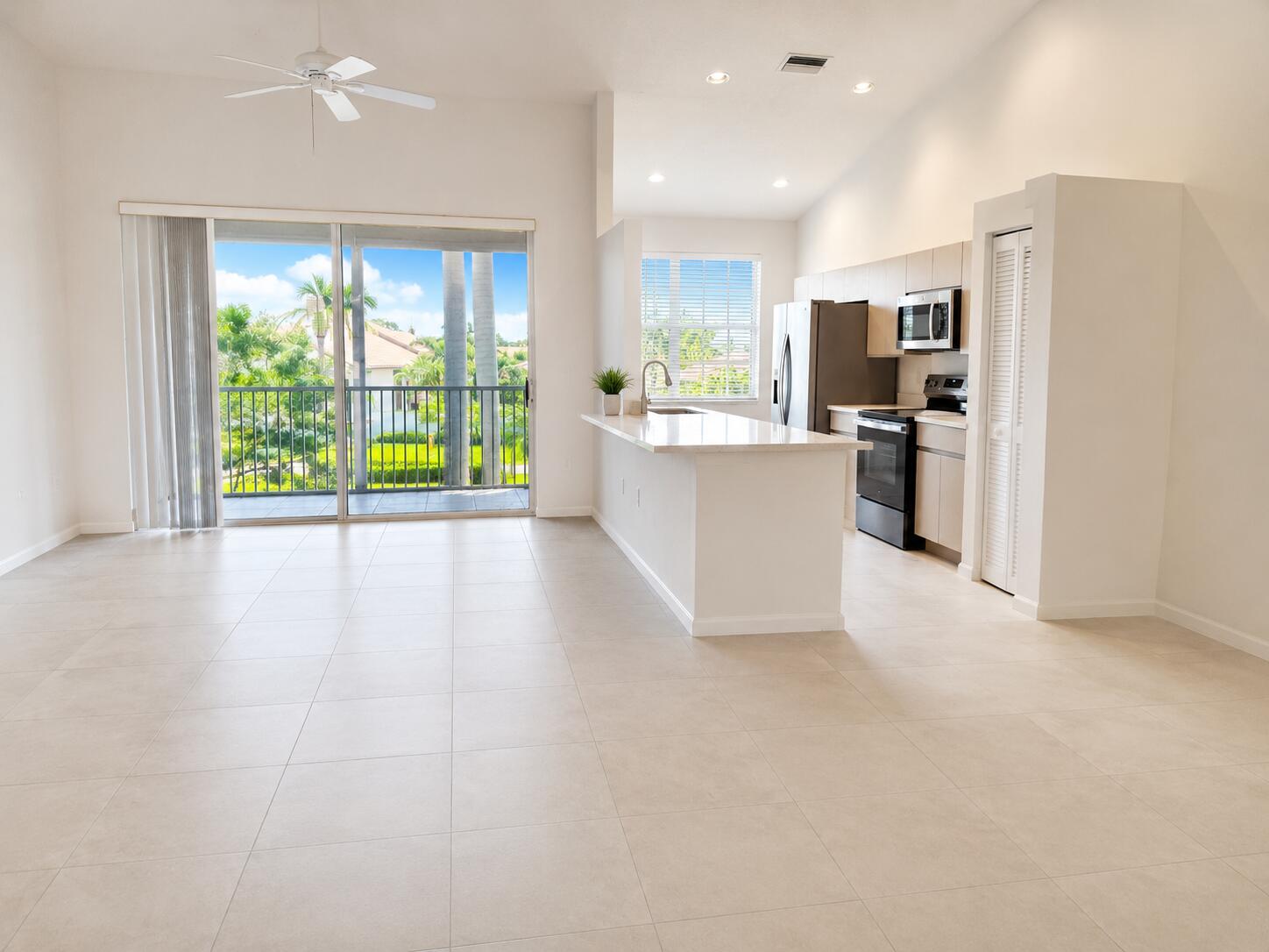Open floor plan featuring large-format tile flooring, a kitchen island with stone-finish countertops, vaulted ceilings, and a sliding glass door opening to a private balcony
