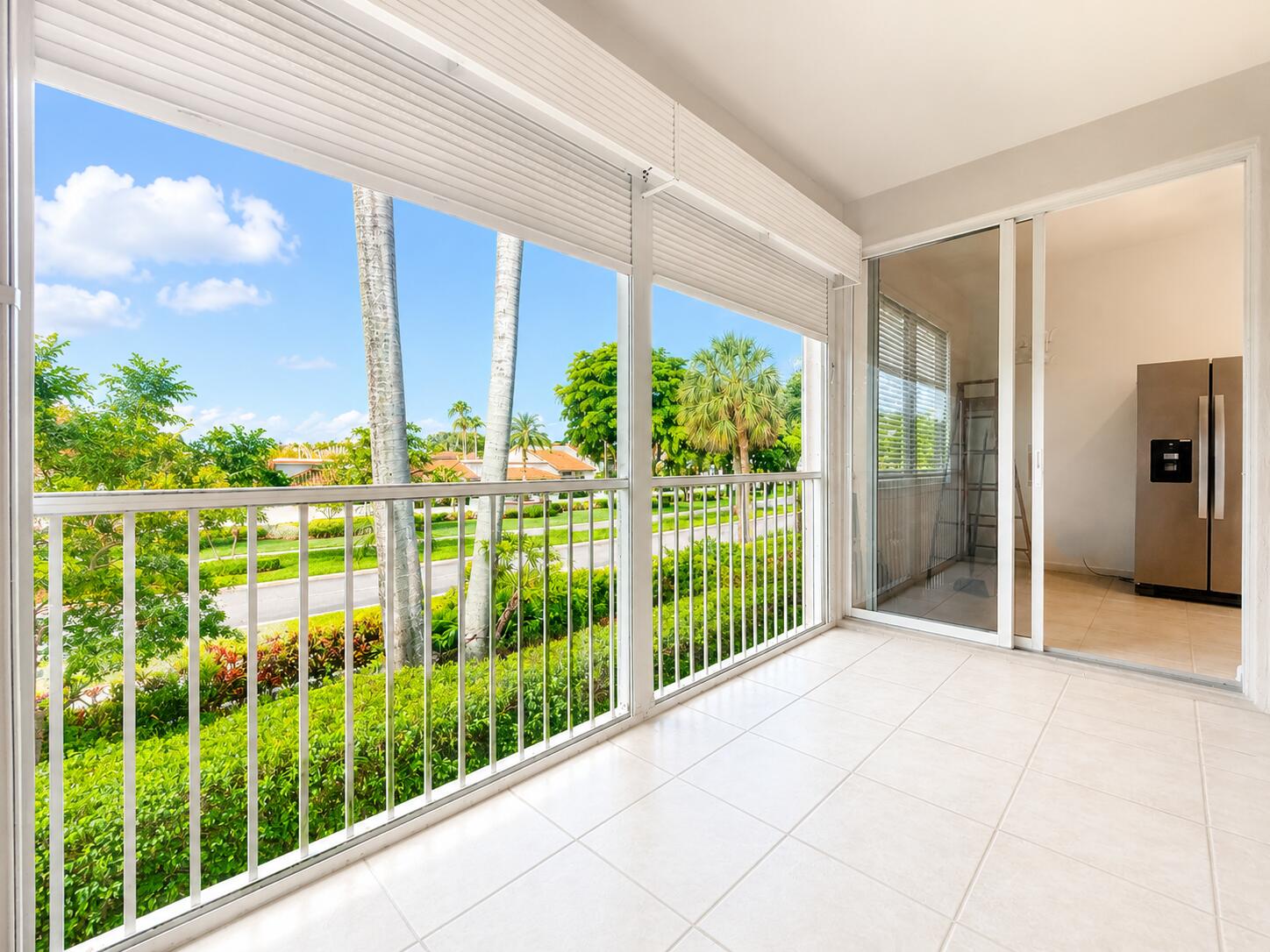 Enclosed balcony featuring white tile flooring, aluminum railings, overhead roll-down shutters, and sliding glass entry doors