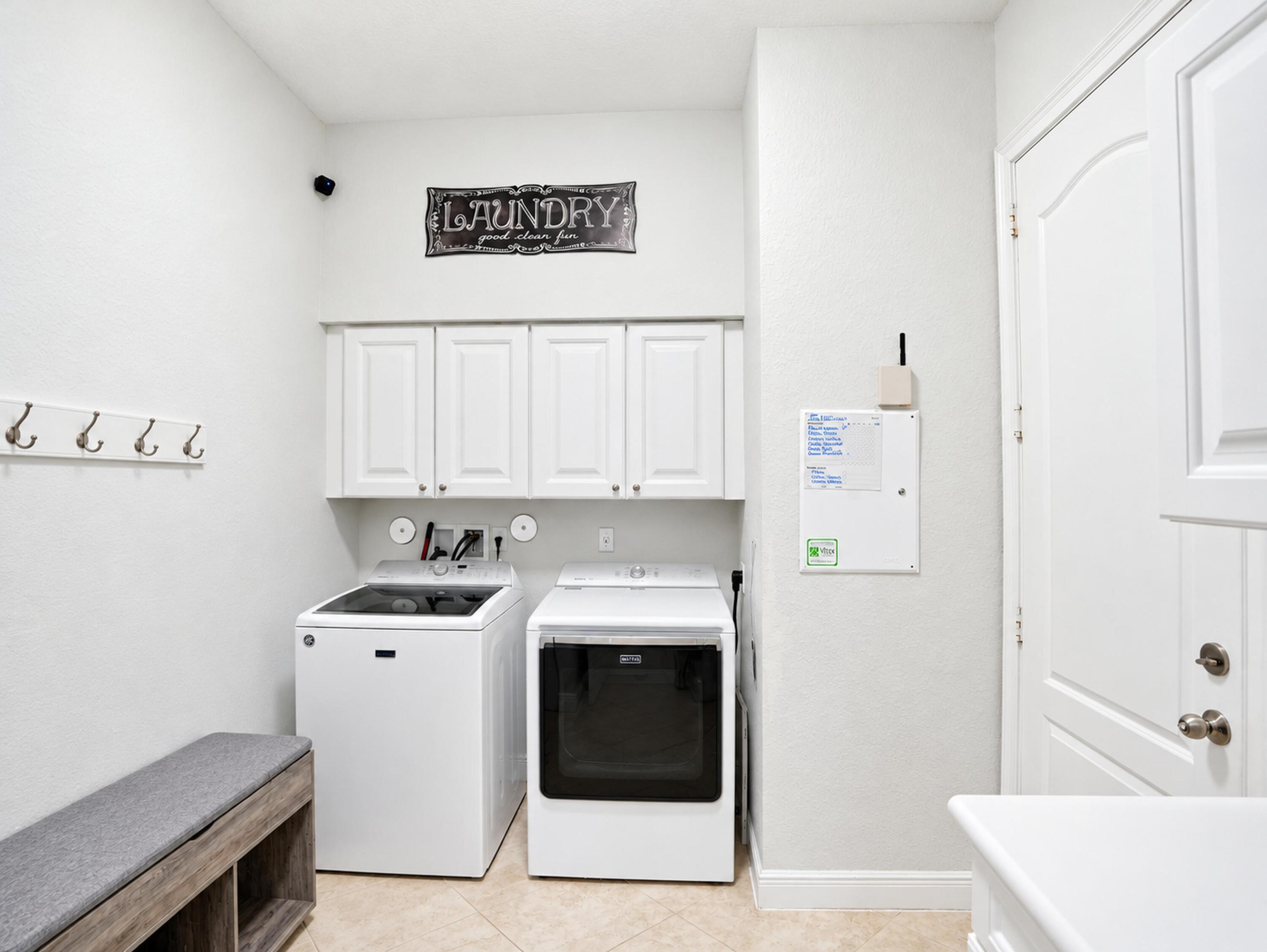 Laundry area featuring upper white cabinetry, wall-mounted coat hooks, and neutral tile flooring