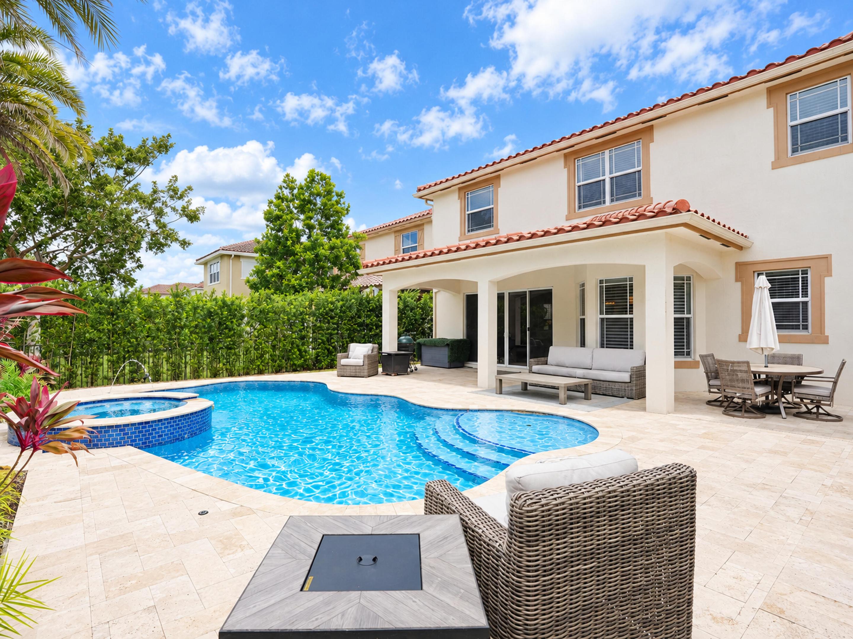 Exterior stucco residence featuring a tile roof, covered patio, stone paver decking, and a pool with an integrated spa