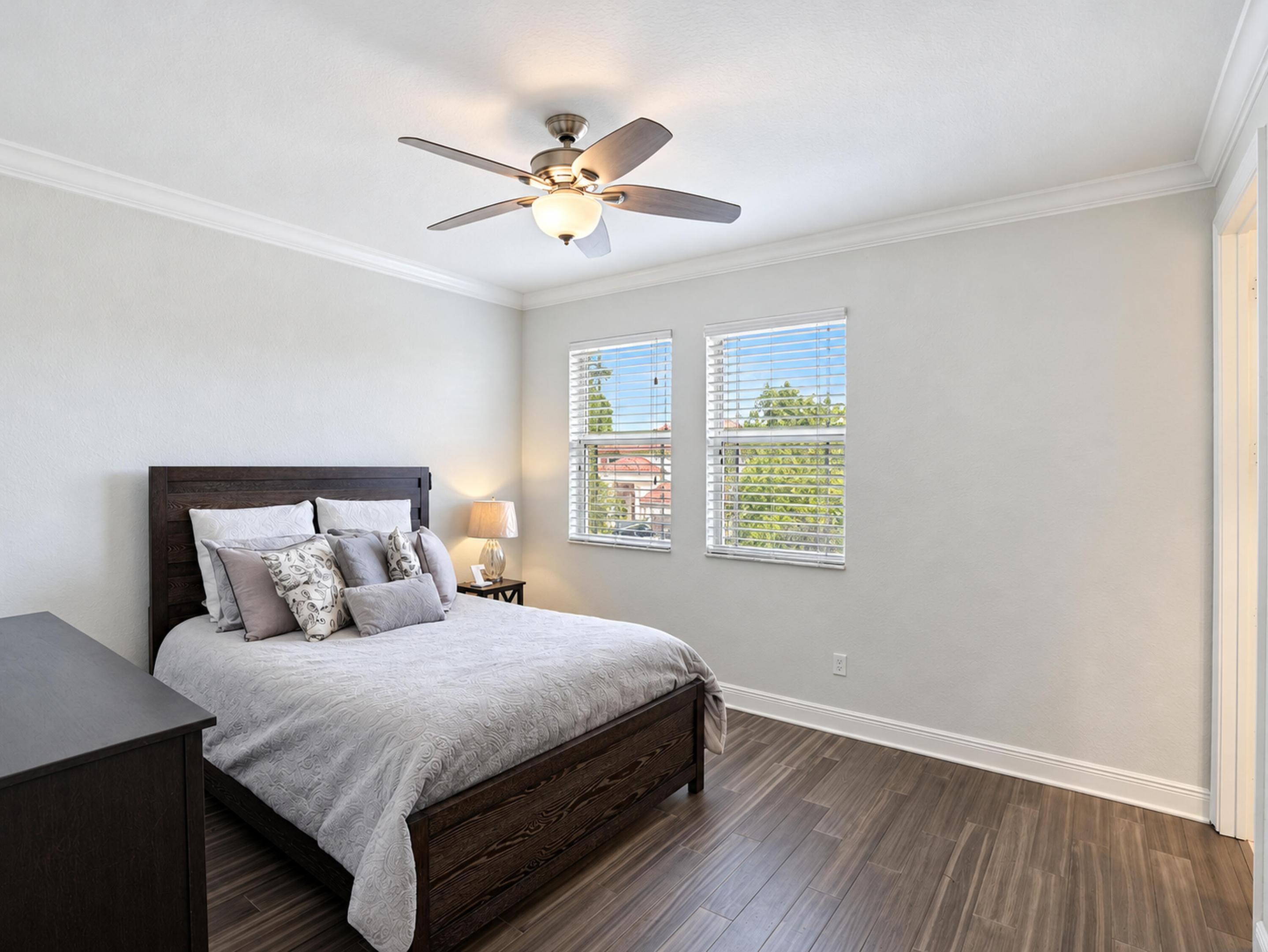Room featuring wood-finish flooring, crown molding, dual windows with horizontal blinds, and a centrally mounted ceiling fan with integrated lighting