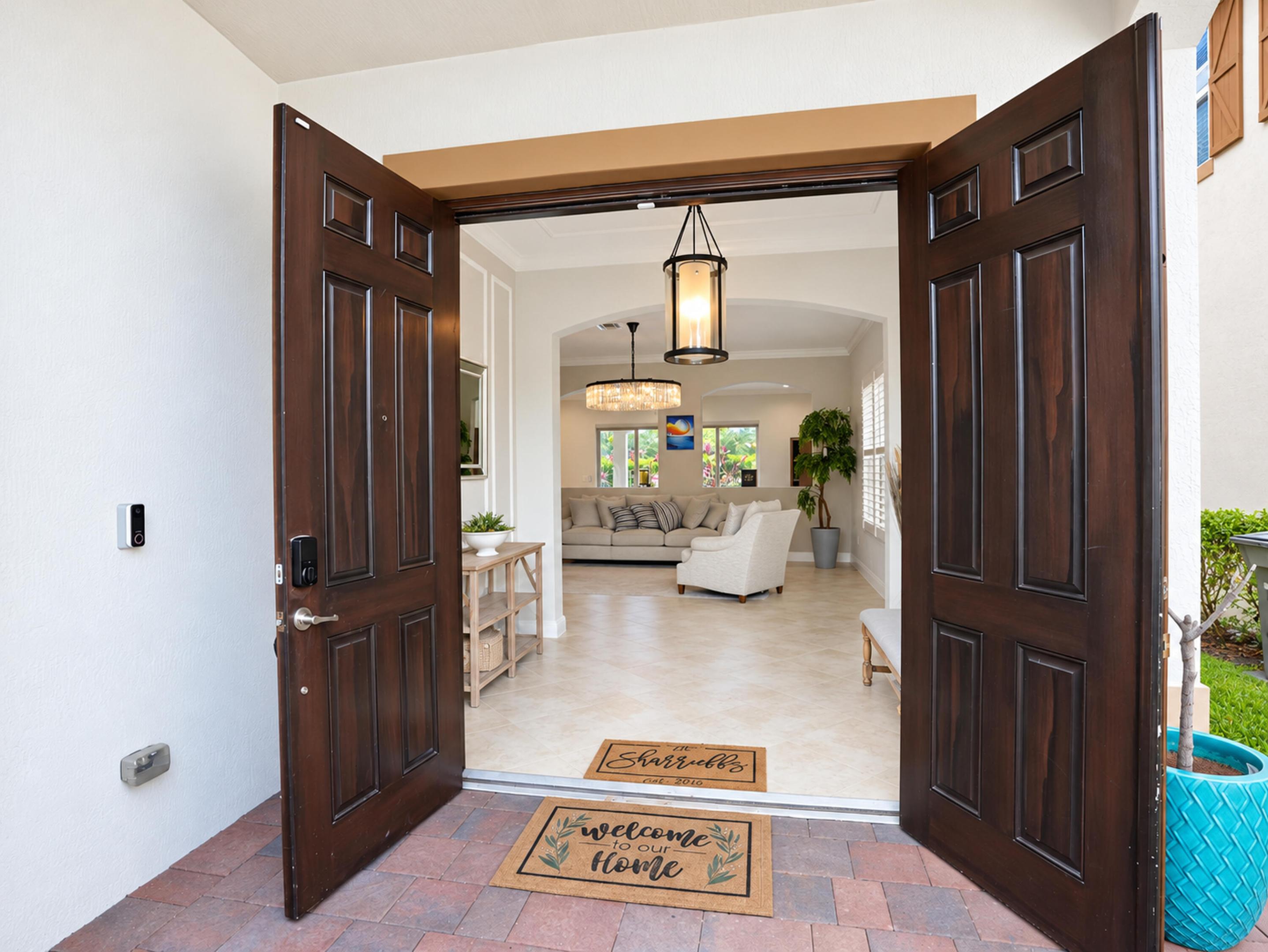 Double entry door featuring dark wood-finish paneled doors and stone-paver flooring at the threshold, complemented by a hanging pendant light fixture and arched entryway