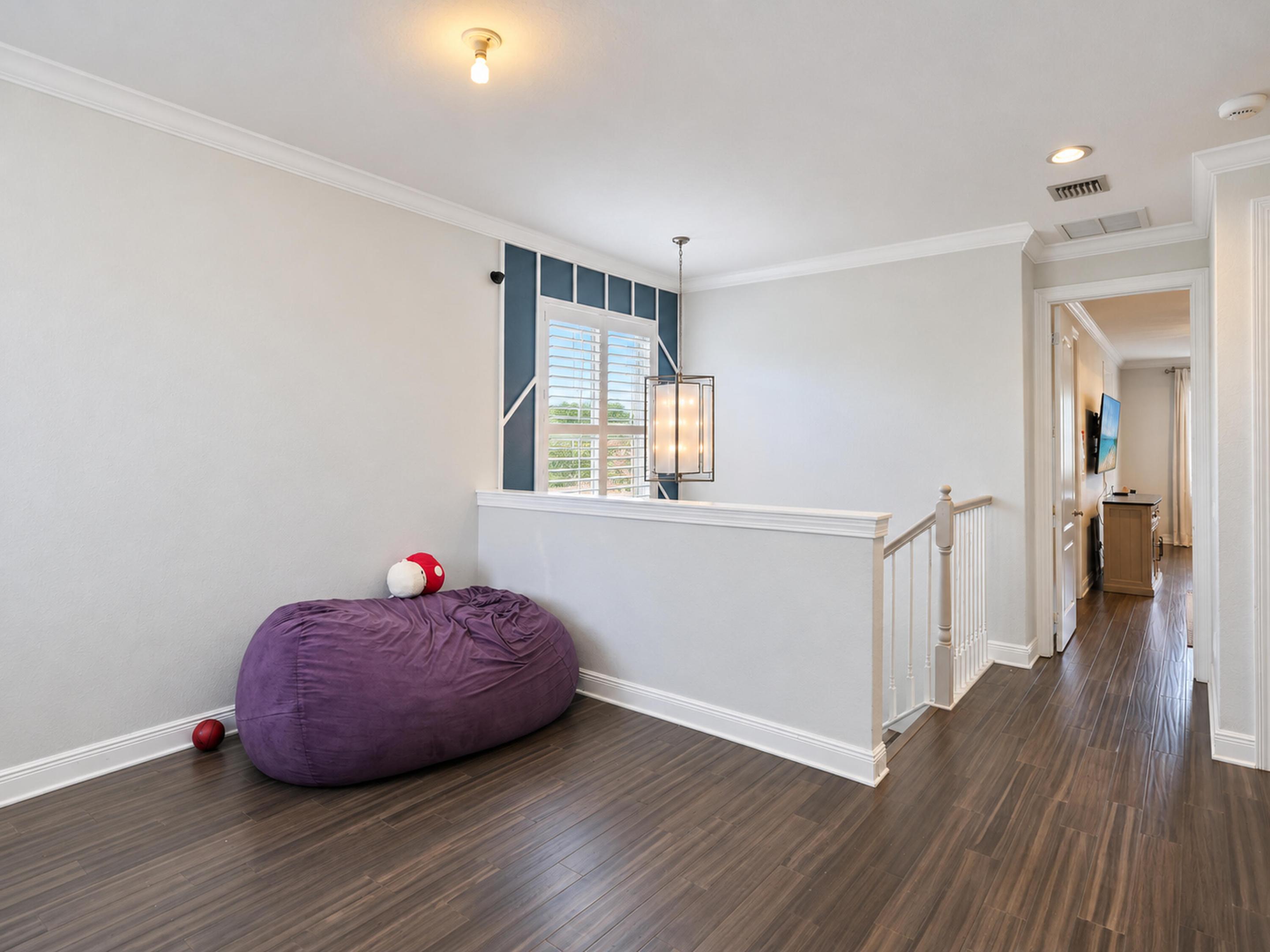 Interior space featuring wood-finish flooring, crown molding, a hanging pendant light fixture, plantation shutters, and a stairwell with a painted wood balustrade