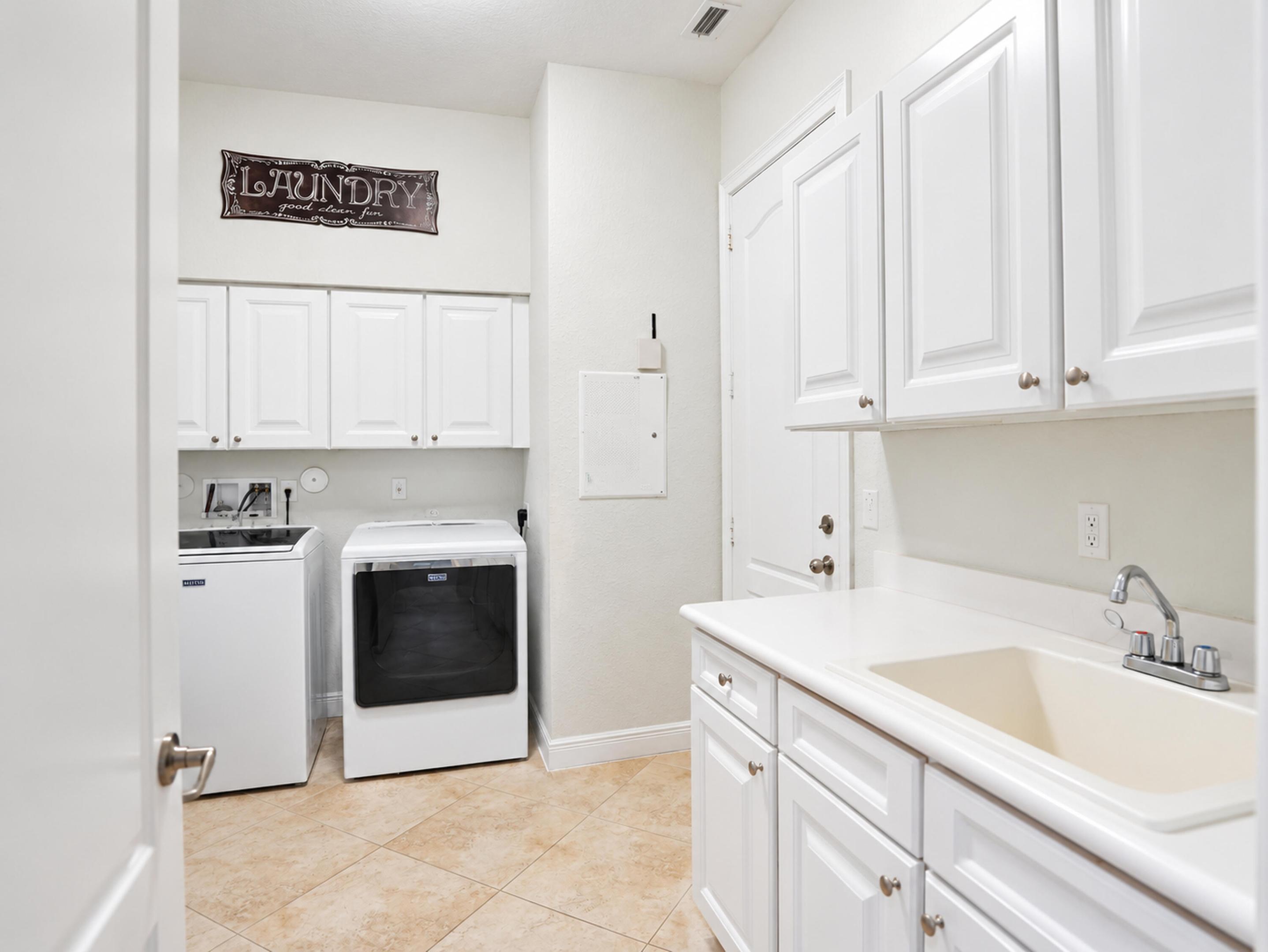 Laundry room featuring white cabinetry, stone-finish tile flooring, a built-in utility sink with a chrome faucet, and ample wall-mounted storage cabinets