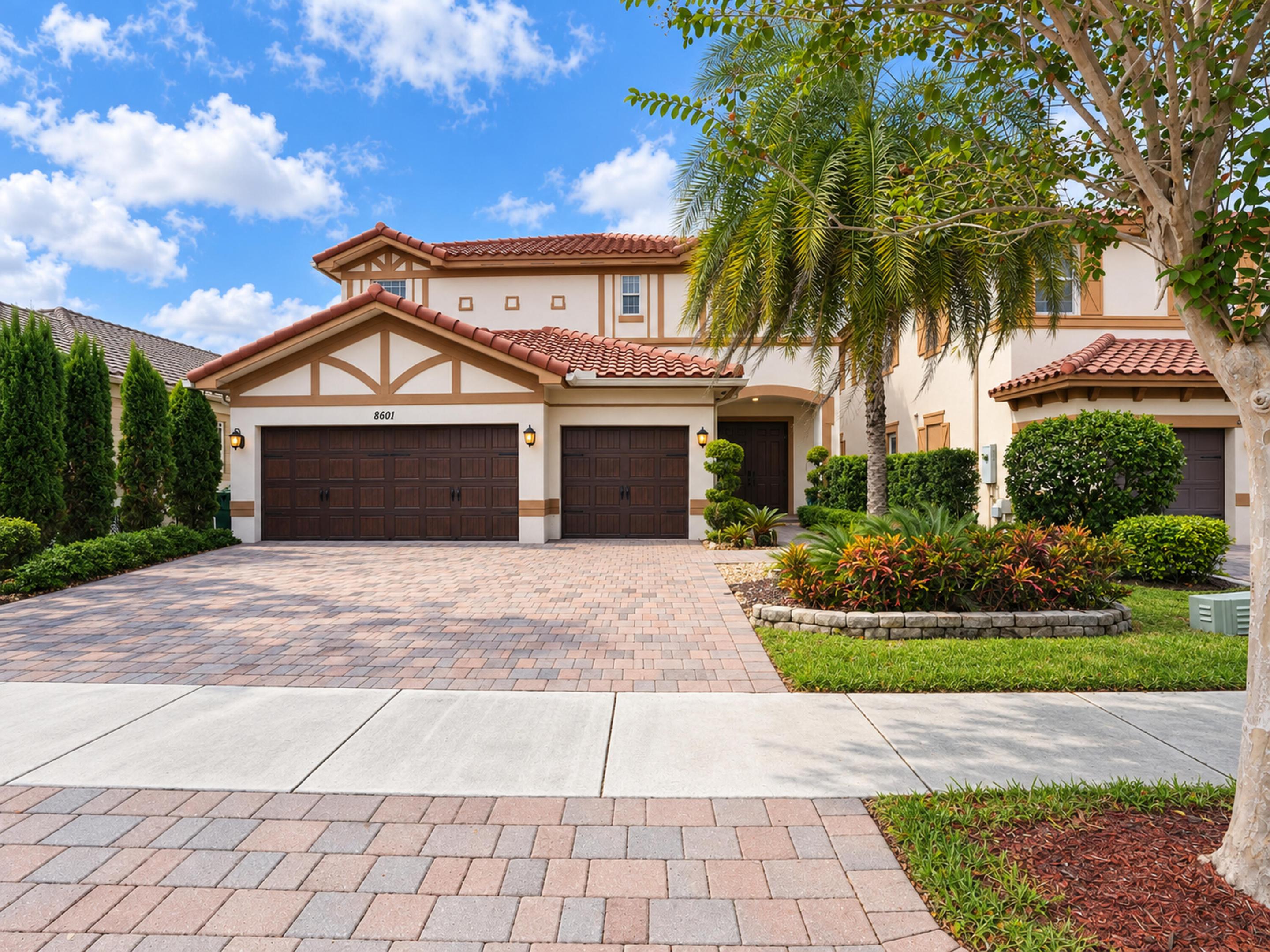 Stucco exterior featuring a clay tile roof, three-car garage, and paver driveway with integrated landscaping