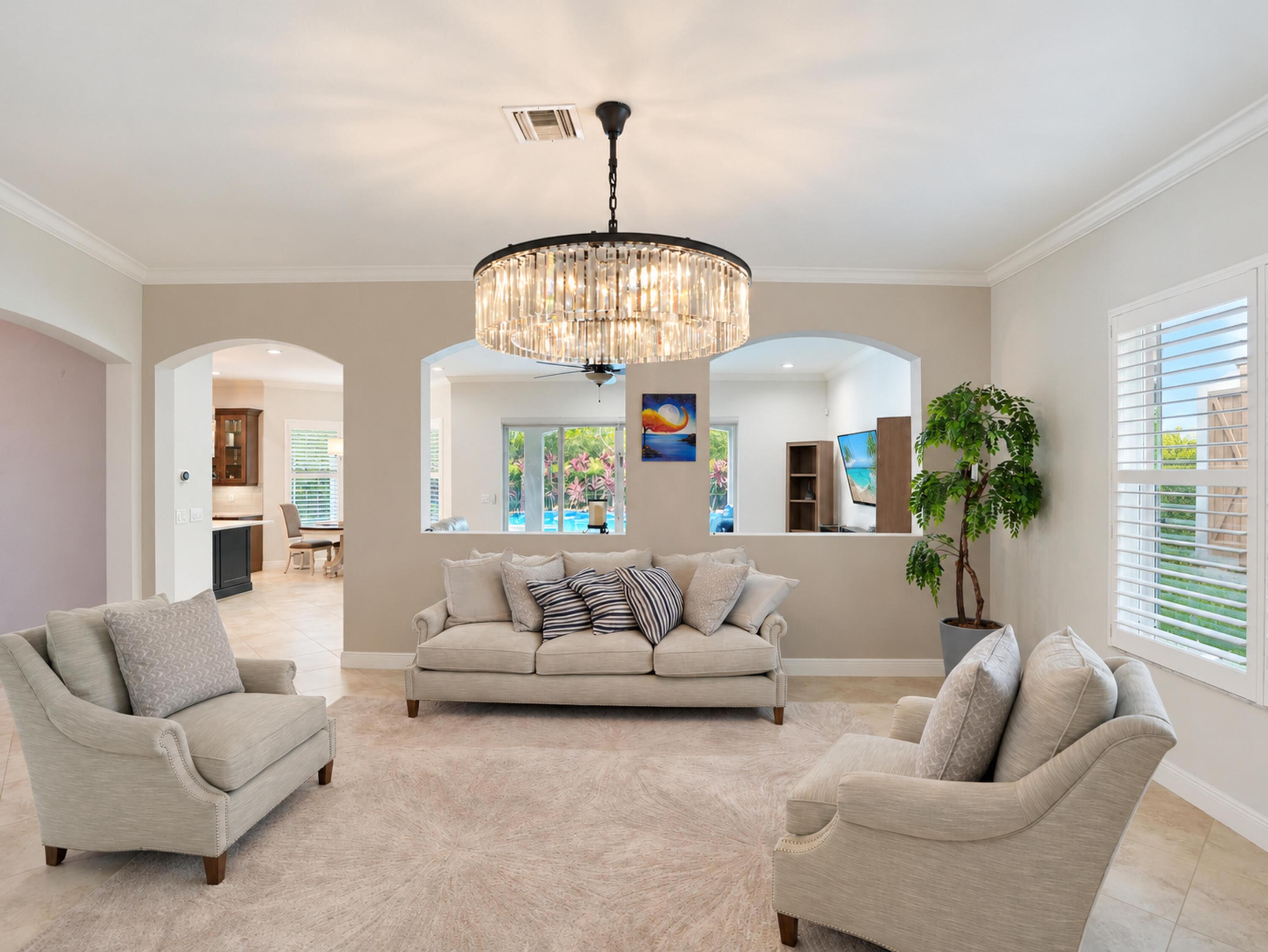 Living space featuring a large-scale drum chandelier with crystal accents, dual arched wall cutouts, crown molding, and plantation shutters