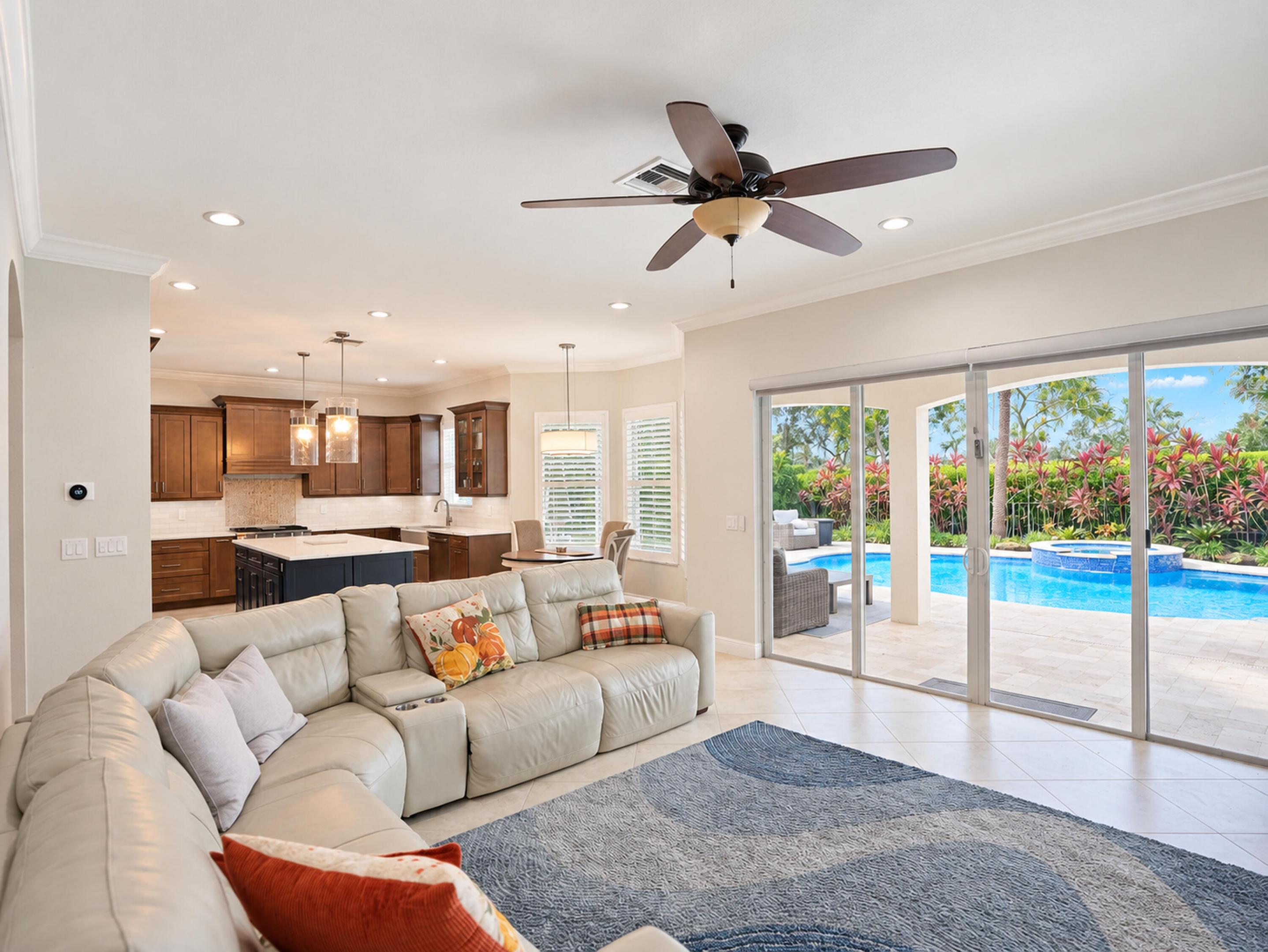 Open-concept living space featuring wood-finish cabinetry, center kitchen island, recessed lighting, and large sliding glass doors opening to a private pool and patio area