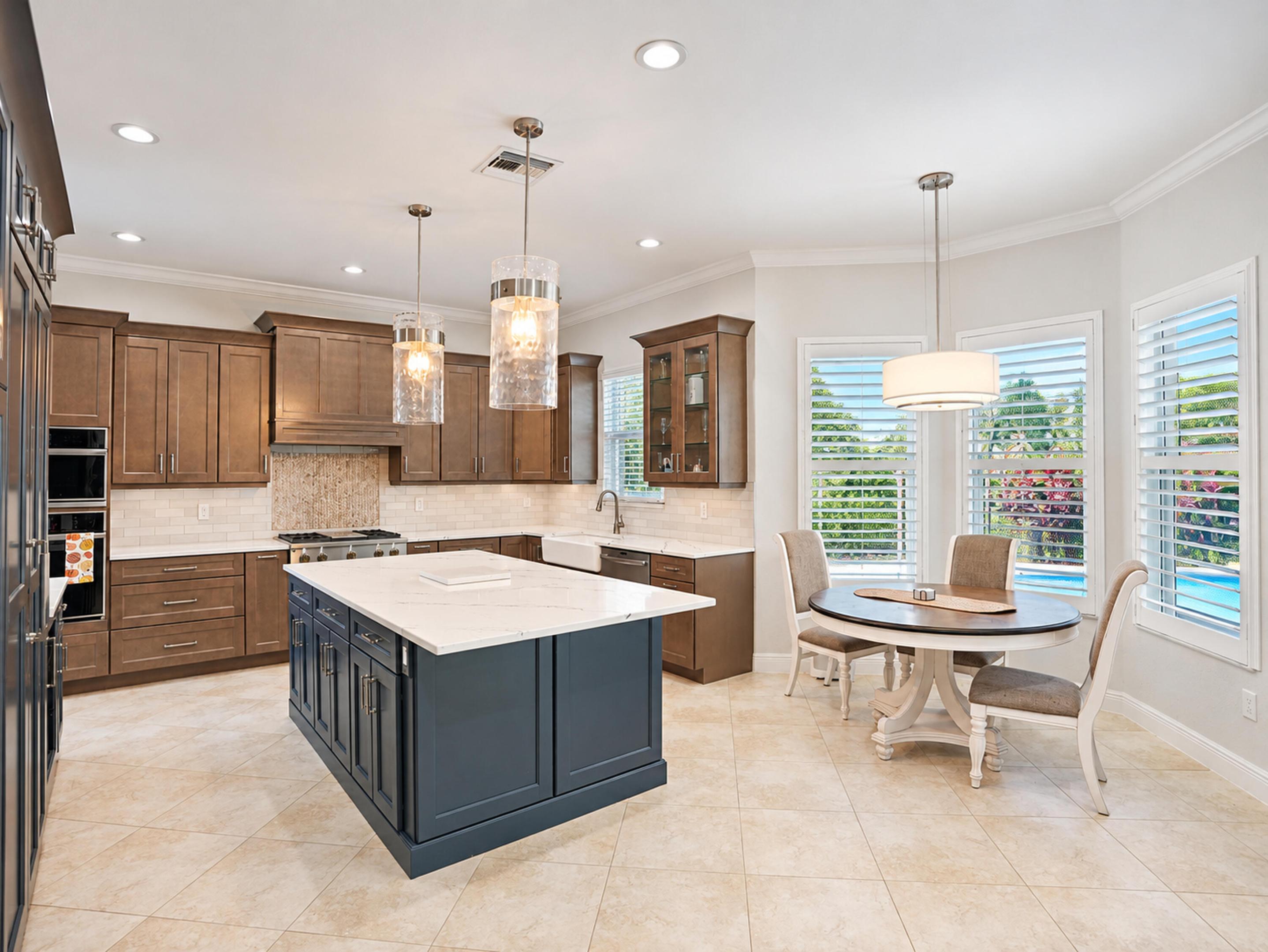 Kitchen featuring custom wood cabinetry, central island with contrasting finish and stone-composite countertop, farmhouse sink, integrated double wall ovens, and recessed lighting