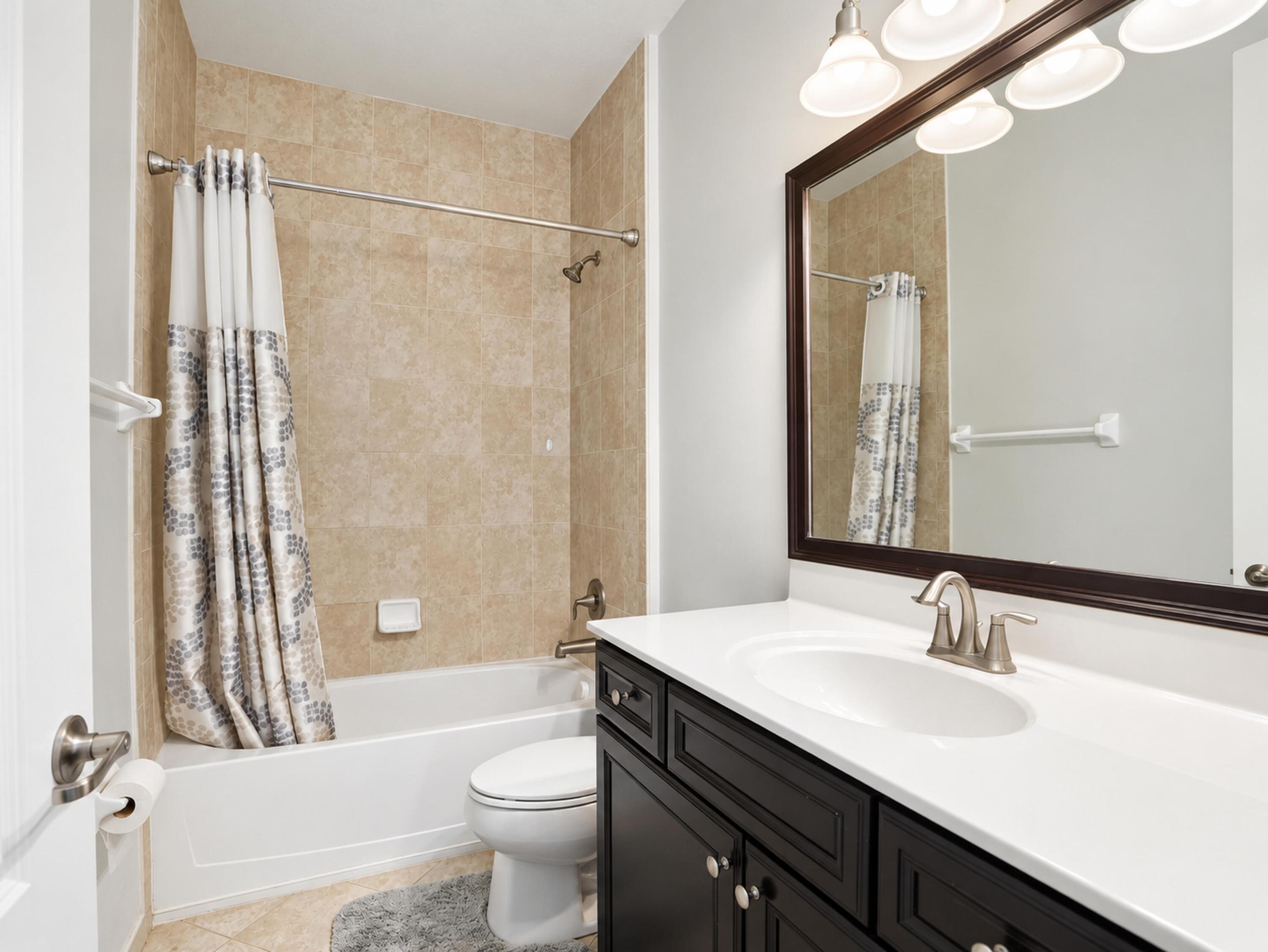 Full bathroom featuring a dark wood vanity with a white countertop, an undermount sink with a brushed nickel faucet, a framed mirror, and a tub-shower combination with tiled surround