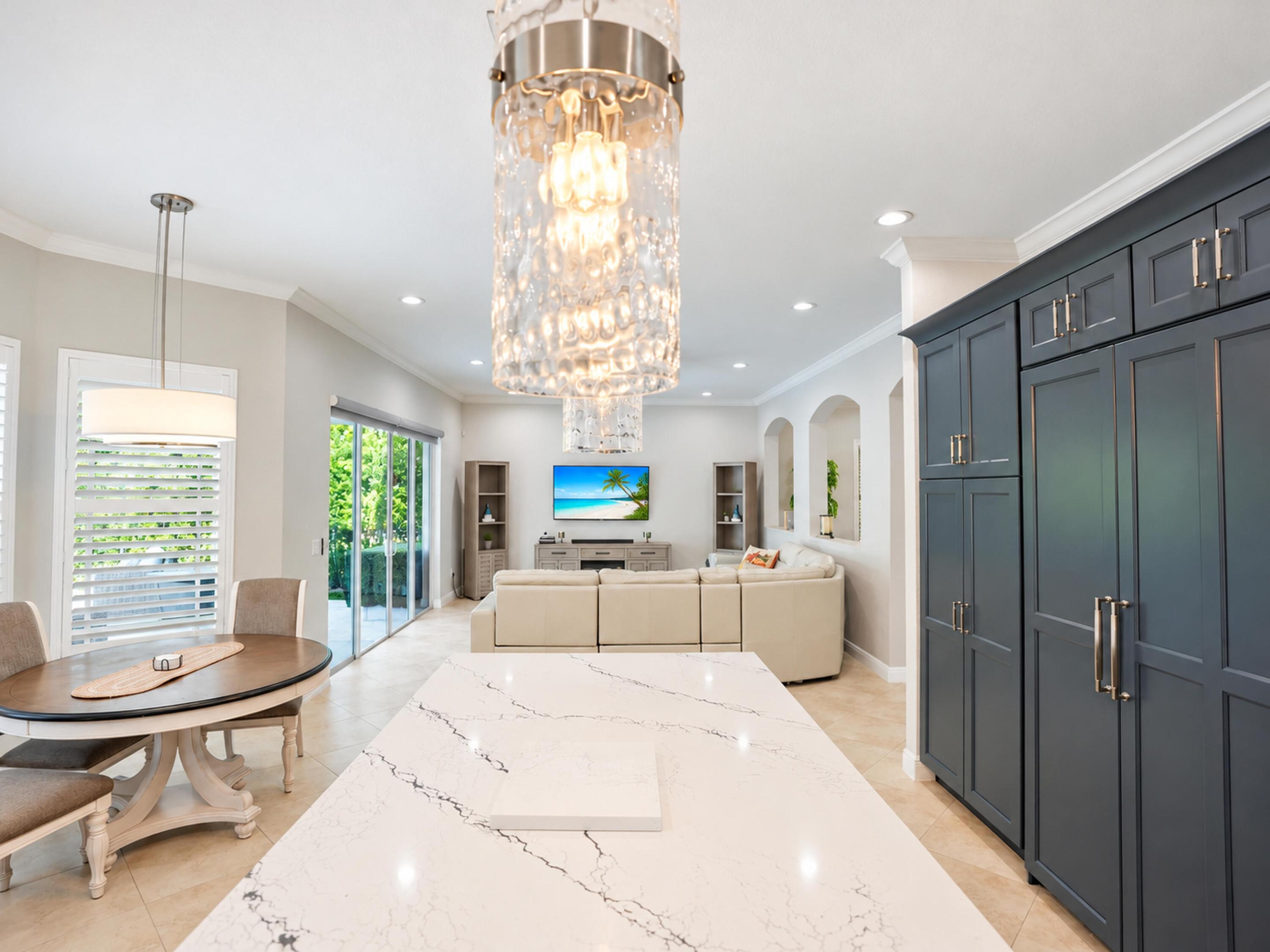 Large kitchen island with a stone countertop, floor-to-ceiling dark cabinetry, crystal statement lighting, recessed ceiling lights, and tile flooring