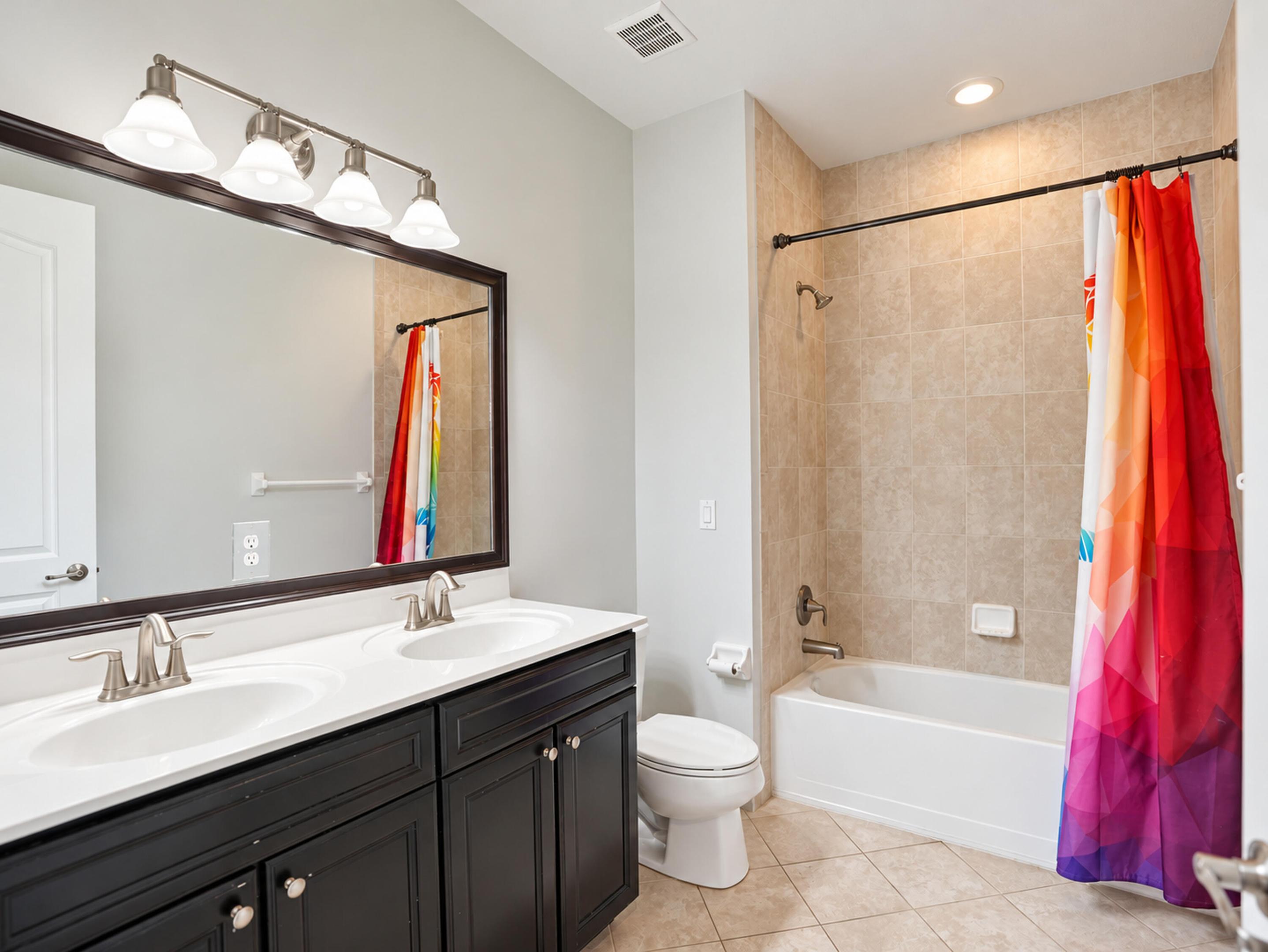 Double vanity featuring dark cabinetry, solid surface countertops with dual integrated sinks, four-light vanity fixture, and tiled tub and shower combination