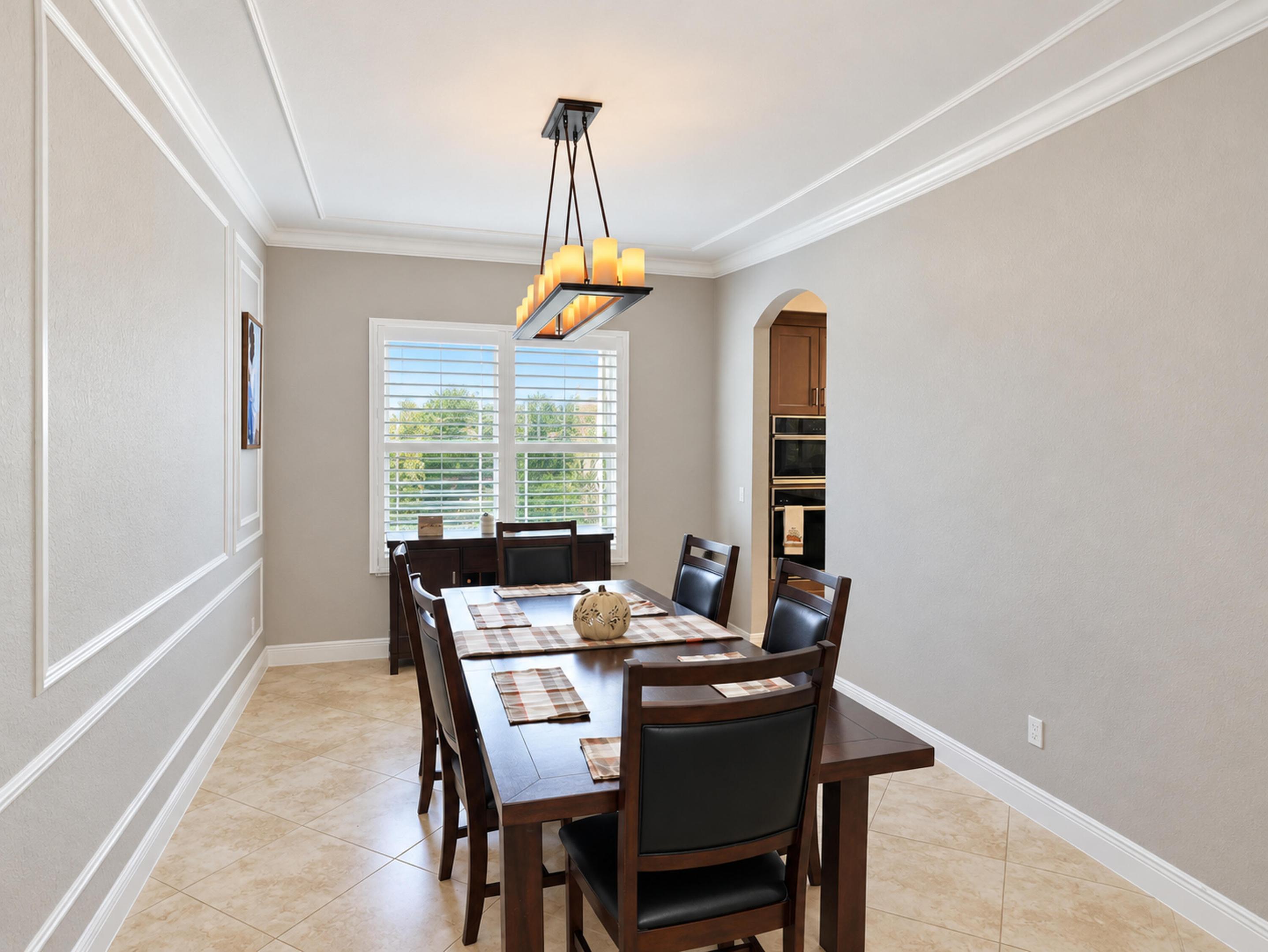 Dining area featuring crown molding, wainscot wall paneling, tile flooring, and a multi-light chandelier
