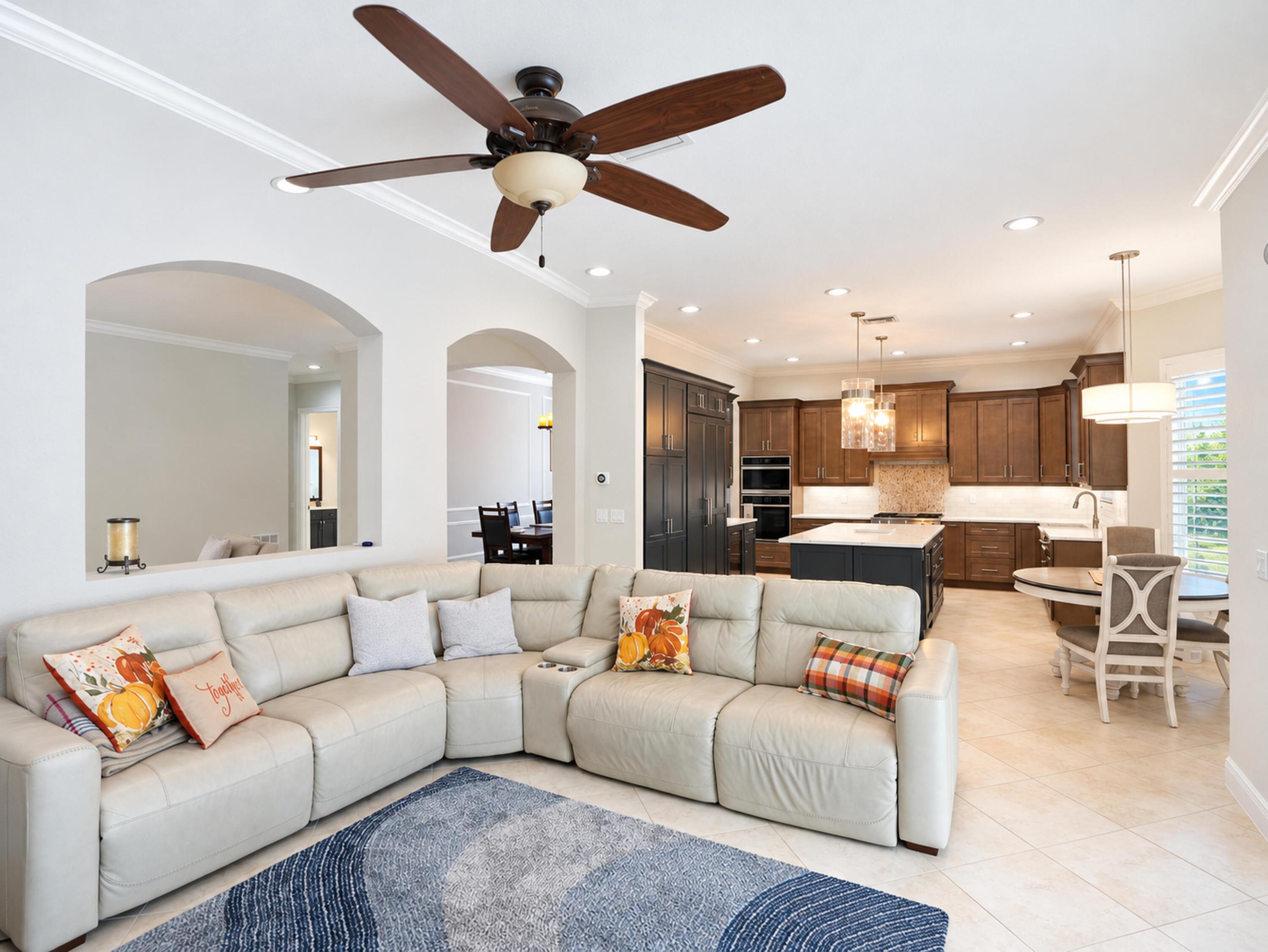 Open-concept living space featuring arched wall cutouts, recessed lighting, multi-tone cabinetry, a central kitchen island with light-toned stone surfacing, and a ceiling fan with integrated lighting