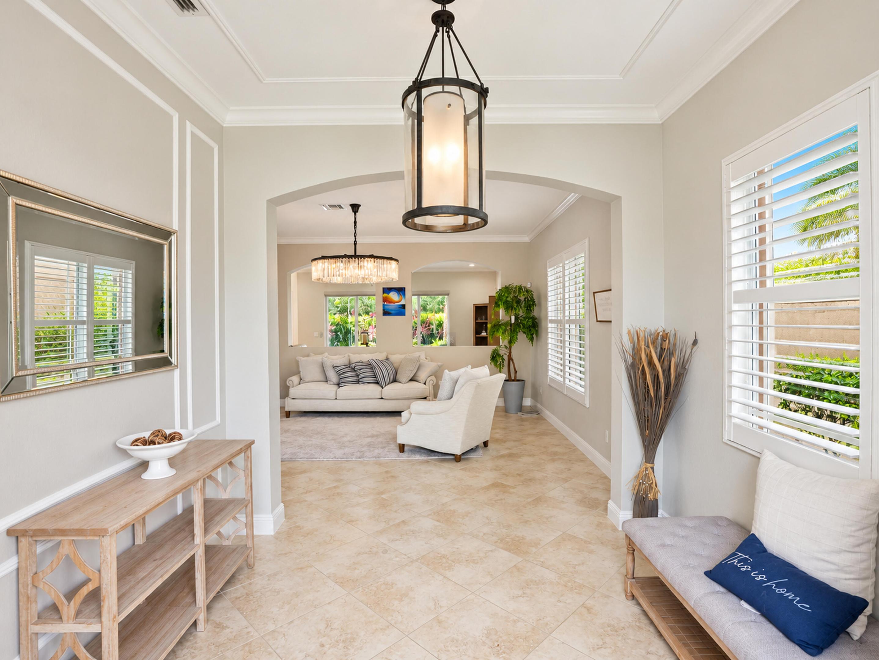 Entryway featuring neutral-toned tile flooring, decorative wall molding, adjustable window shutters, and a prominent cylinder-style hanging light fixture
