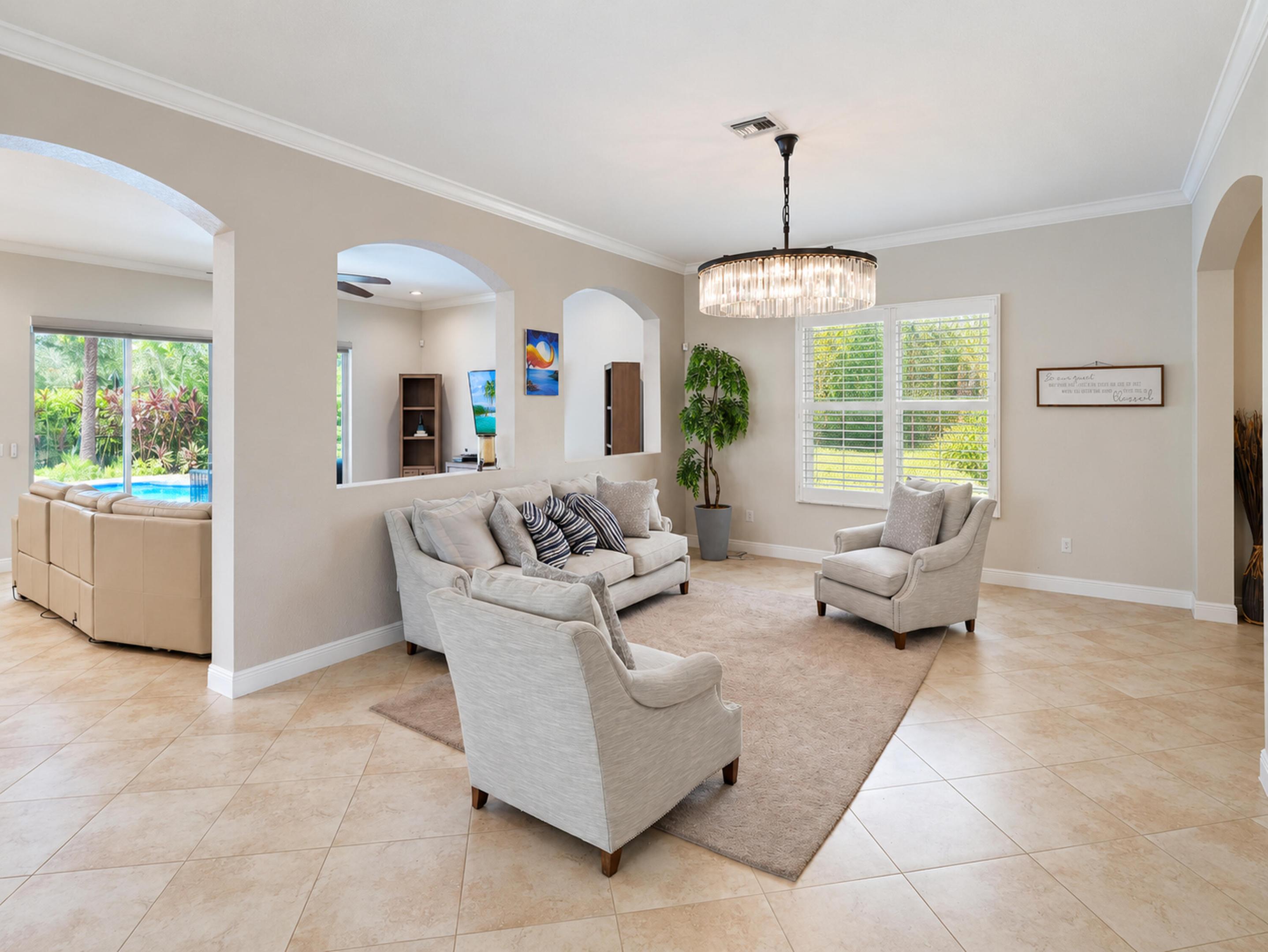 Neutral-toned interior featuring large-format ceramic tile flooring, architectural arched cutouts, crown molding, and a tiered crystal drum chandelier