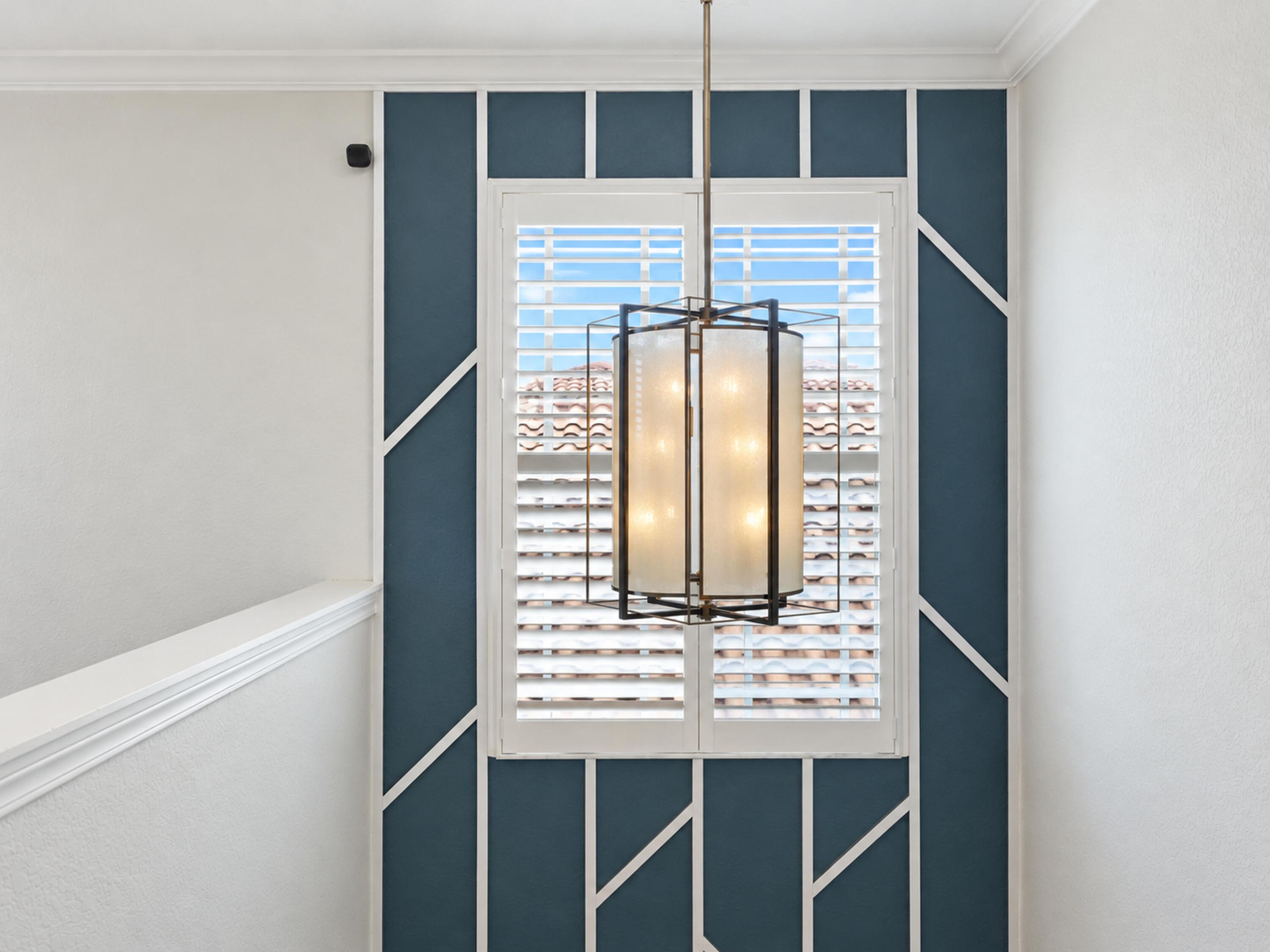 Accent wall with geometric trim detailing, white plantation shutters, and a suspended multi-light pendant fixture