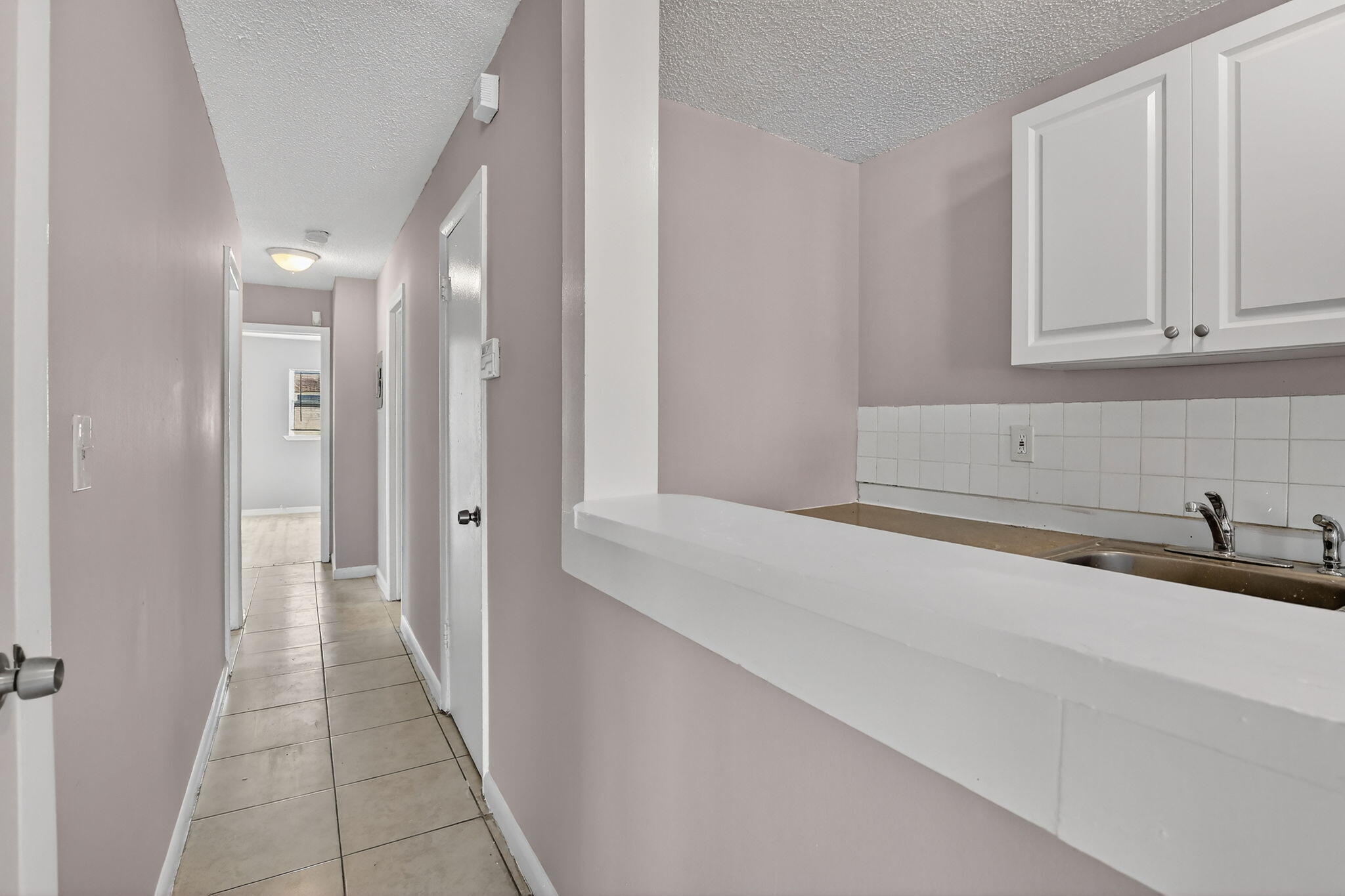 Hallway featuring tile flooring, white shaker-style cabinetry, and a pass-through counter with a tiled backsplash
