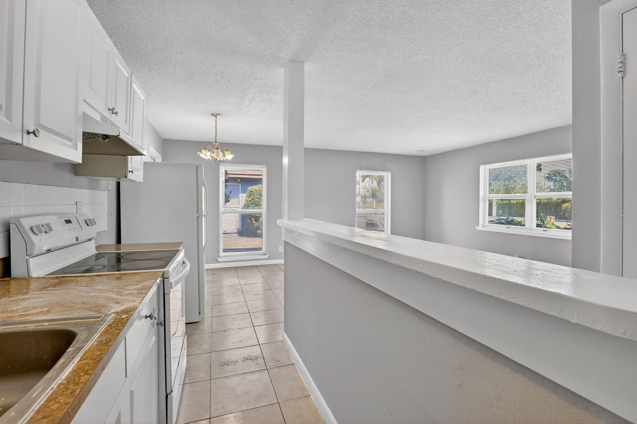 Kitchen featuring white shaker-style cabinetry, stone-finish countertops, tile flooring, and a half-wall partition