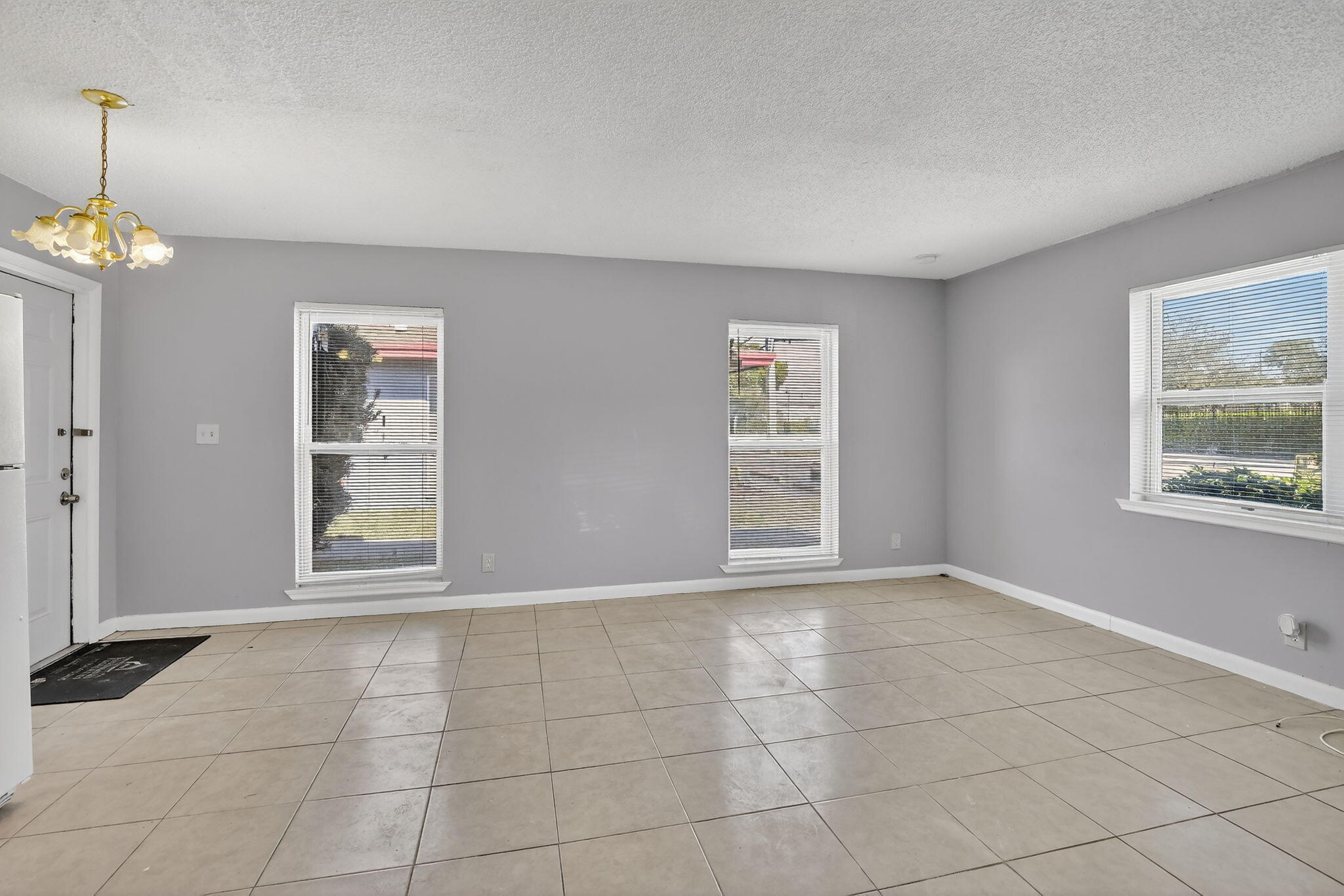 Neutral-toned interior space featuring light-colored ceramic tile flooring, three large windows, and a multi-arm metallic light fixture