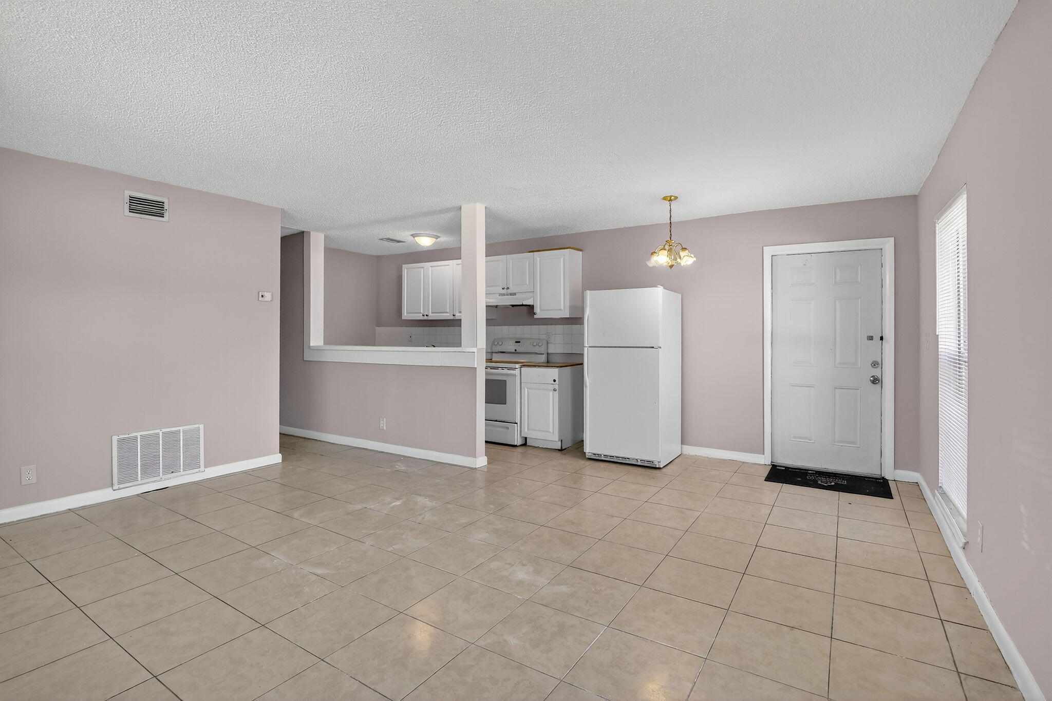 Open-concept interior featuring light-toned tile flooring, white cabinetry, a kitchen pass-through counter, and a six-panel entry door