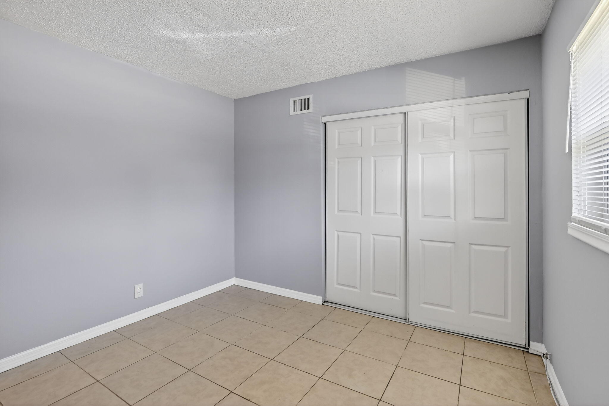 Neutral wall finish, large-format tile flooring, and a double-door sliding closet