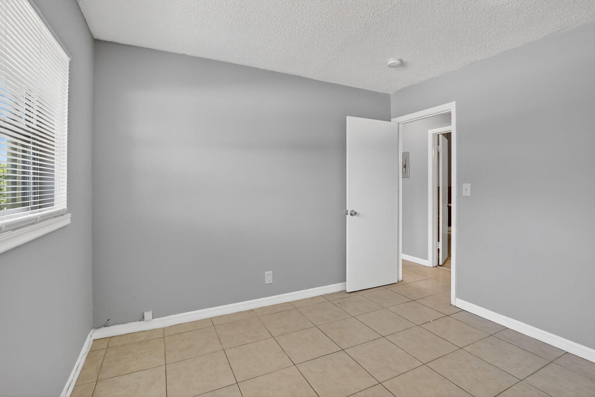 Neutral-toned interior space featuring ceramic tile flooring, painted walls, and a window with white horizontal blinds