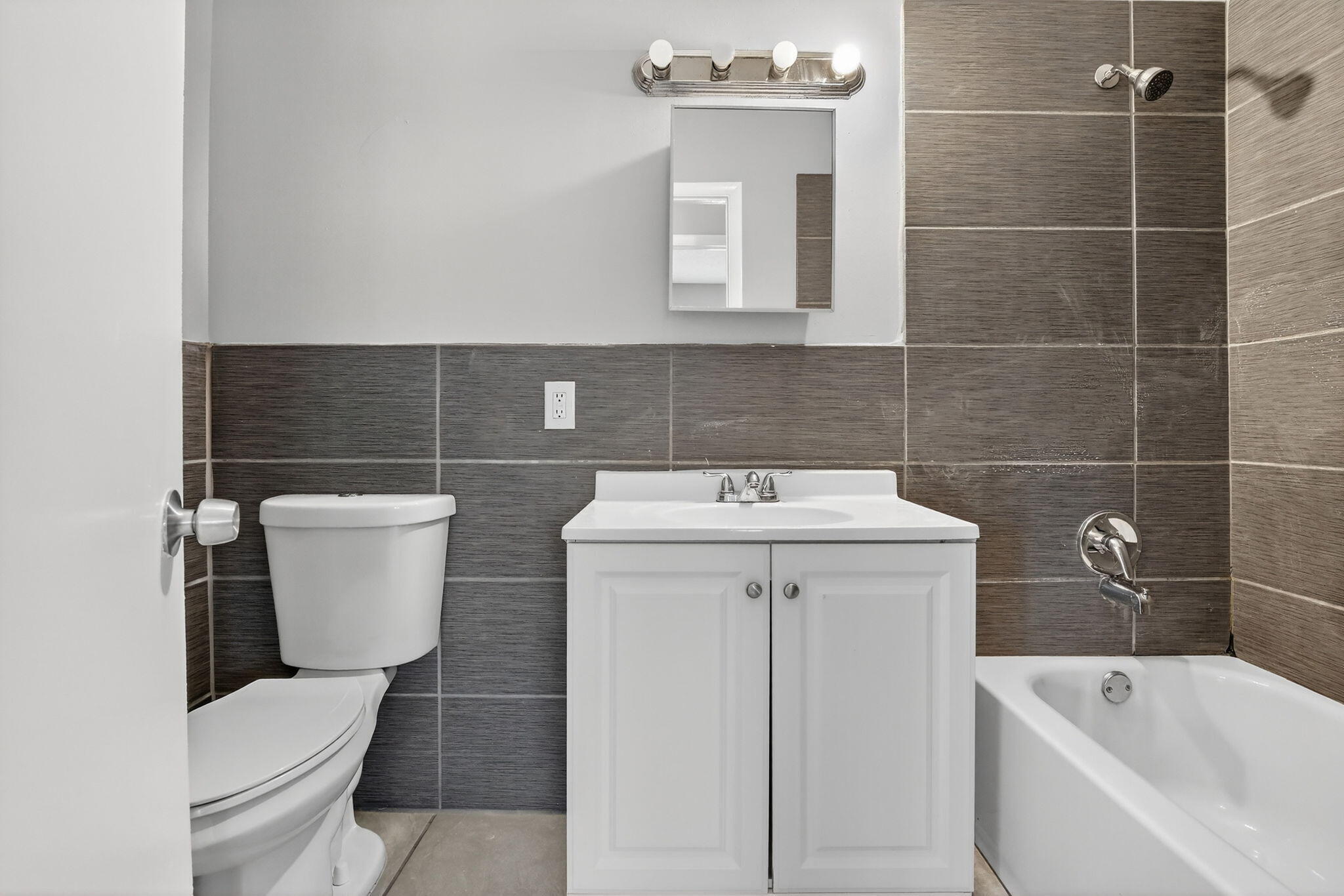Bathroom featuring a white vanity cabinet, rectangular white countertop basin, chrome-finish plumbing fixtures, and large-format gray horizontal wall tile extending into the tub enclosure