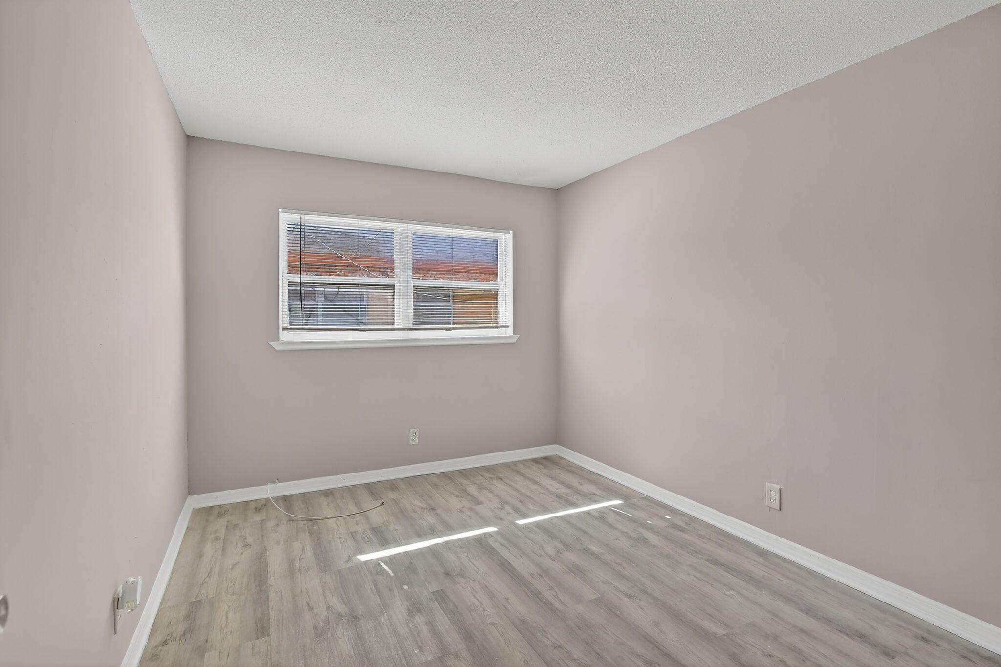 Room featuring neutral-toned walls, wood-finish flooring, and a large picture window with integrated blinds