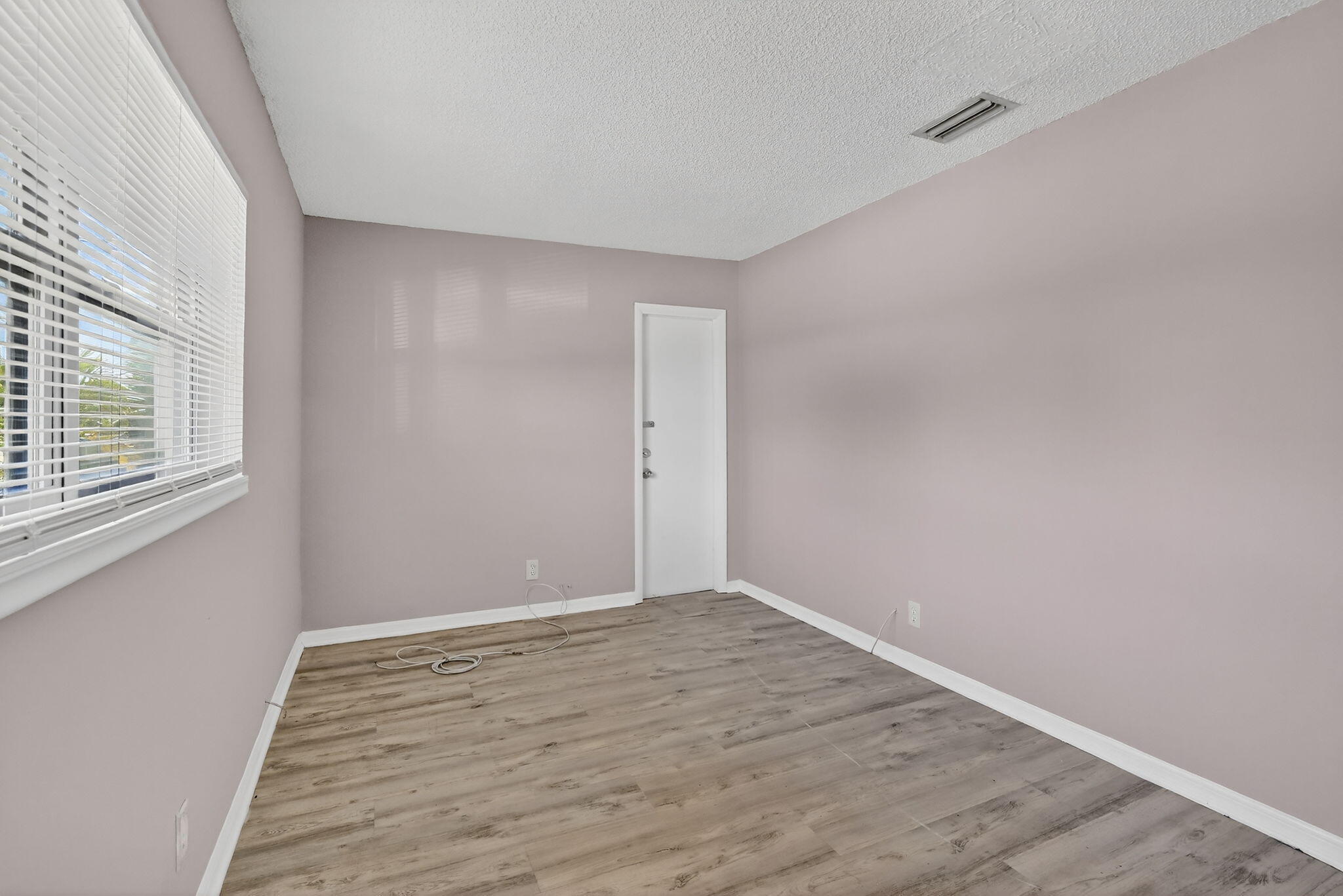 Neutral-toned interior room featuring wood-finish flooring, textured ceiling, and large horizontal window with fitted blinds