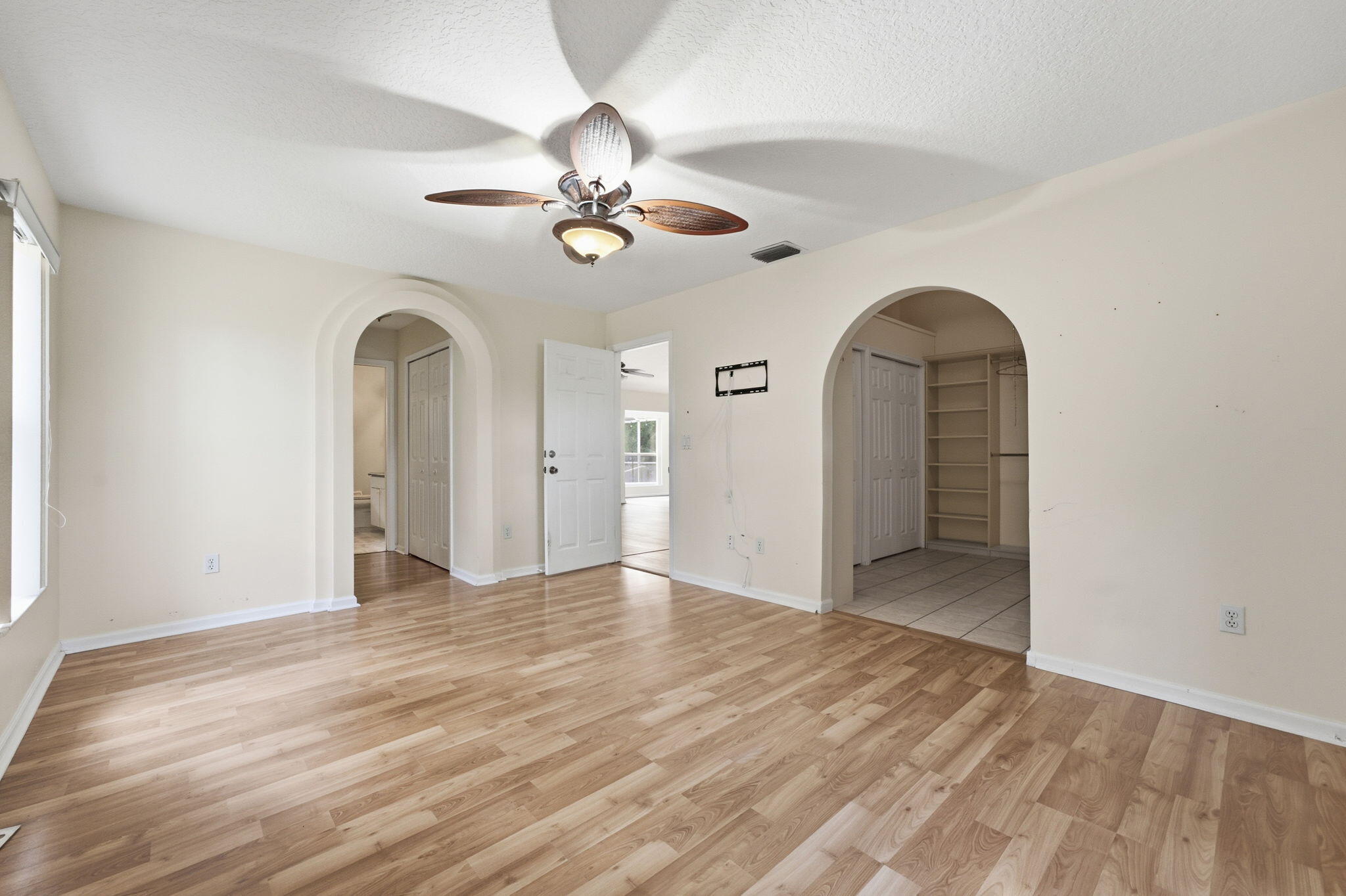 Interior space featuring wood-finish flooring, two arched entryways, ceiling fan with integrated lighting, and built-in shelving