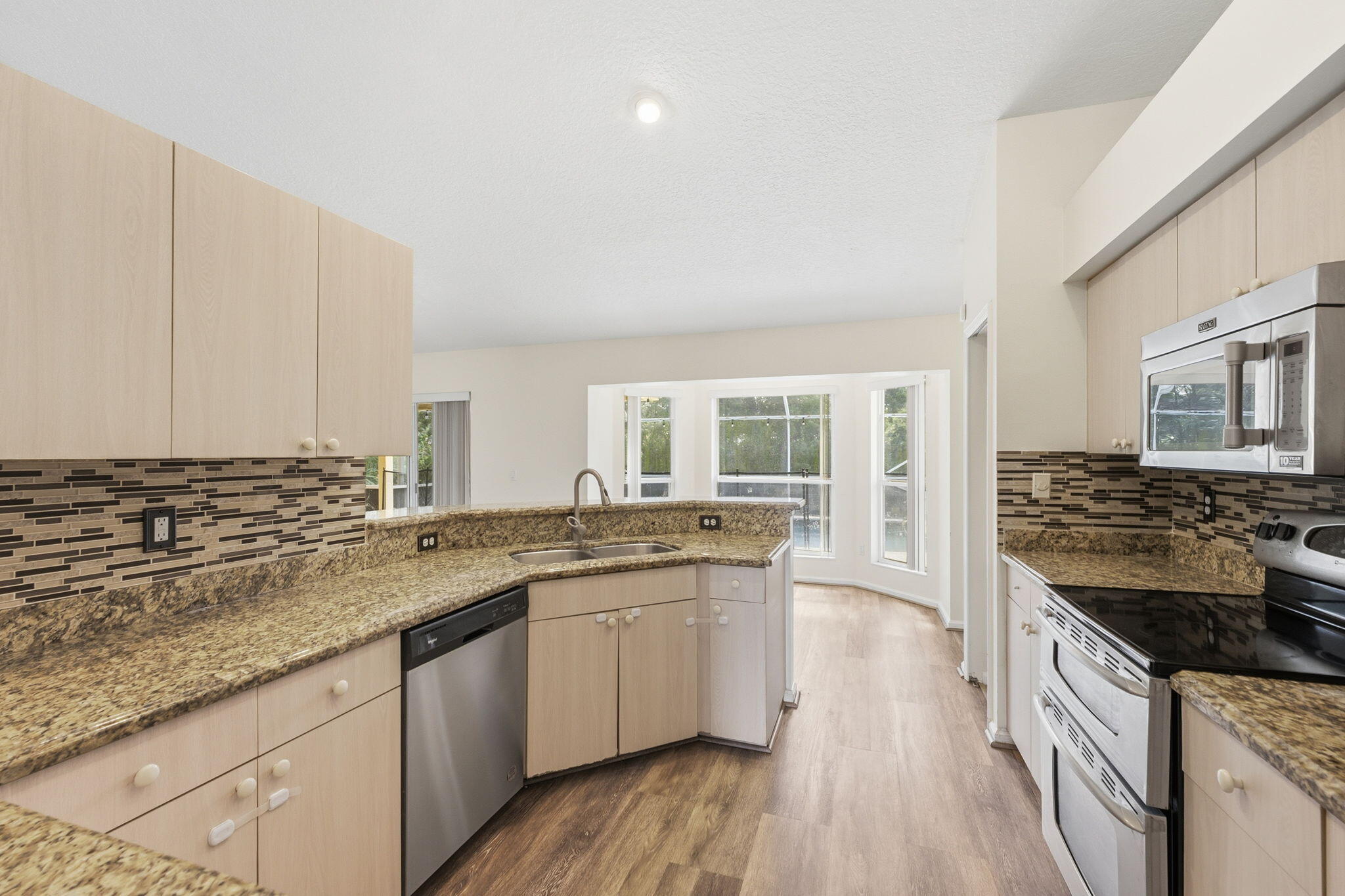 Kitchen featuring light-finish cabinetry, stone-texture countertops, mosaic tile backsplash, wood-finish flooring, and stainless steel appliances