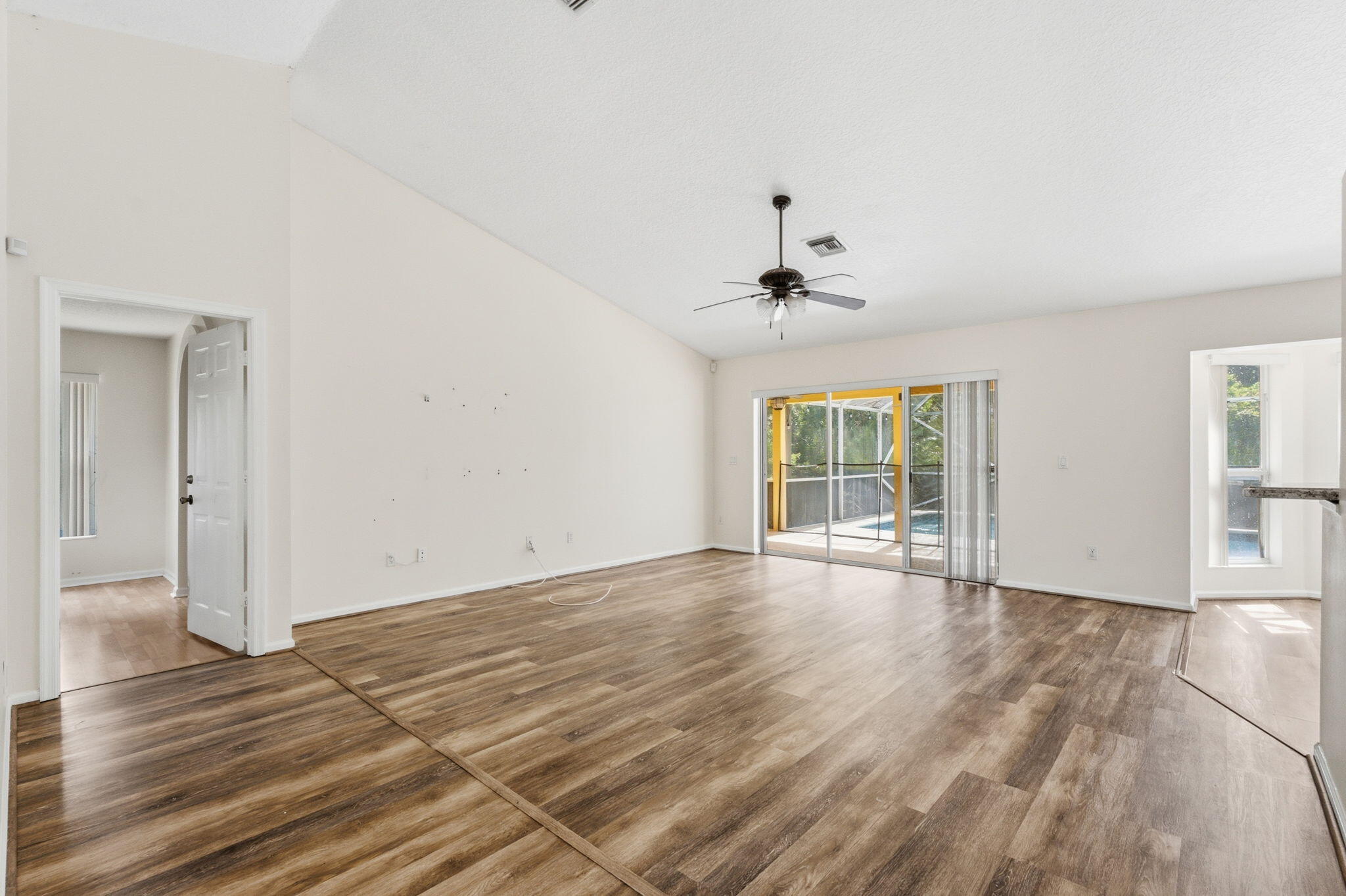 Vaulted ceilings, wood-finish flooring, central ceiling fan, and sliding glass doors providing outdoor access