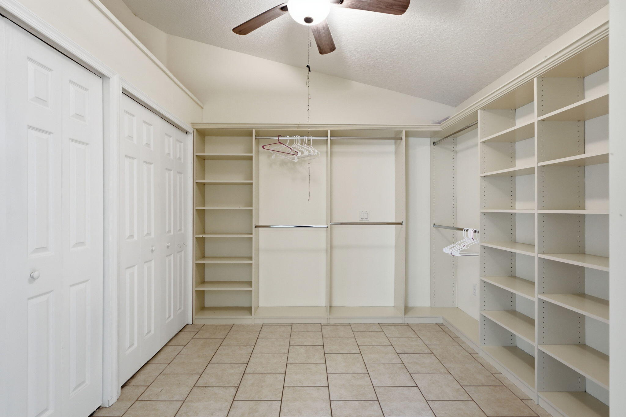 Walk-in closet featuring vaulted ceilings, custom built-in shelving, dual hanging rods, tile flooring, and overhead lighting with an integrated ceiling fan