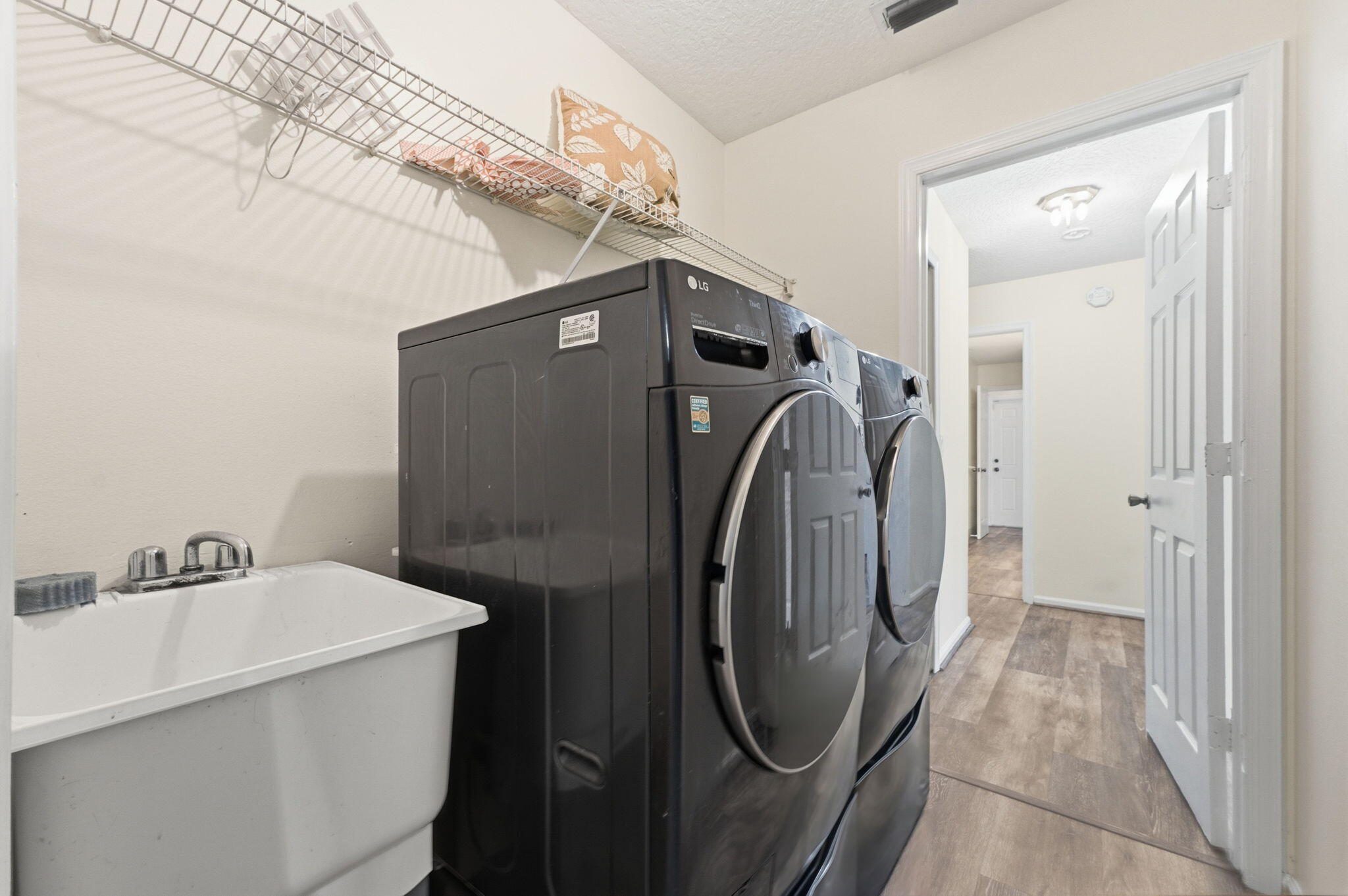 Utility area featuring a deep-basin white sink, chrome faucet hardware, wire shelving, and wood-finish flooring