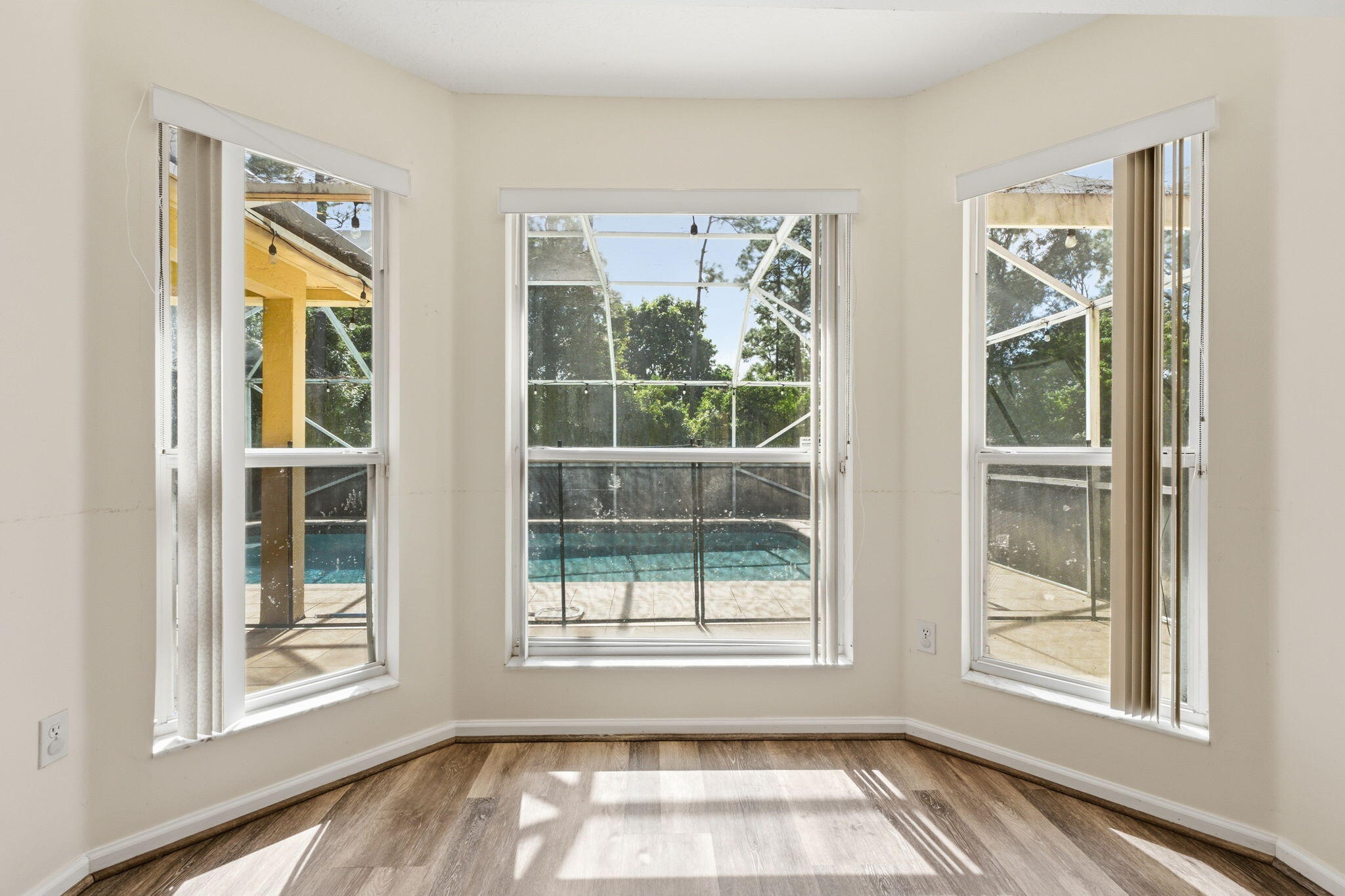 Bay window featuring wood-finish flooring and vertical blinds, showcasing an enclosed pool area