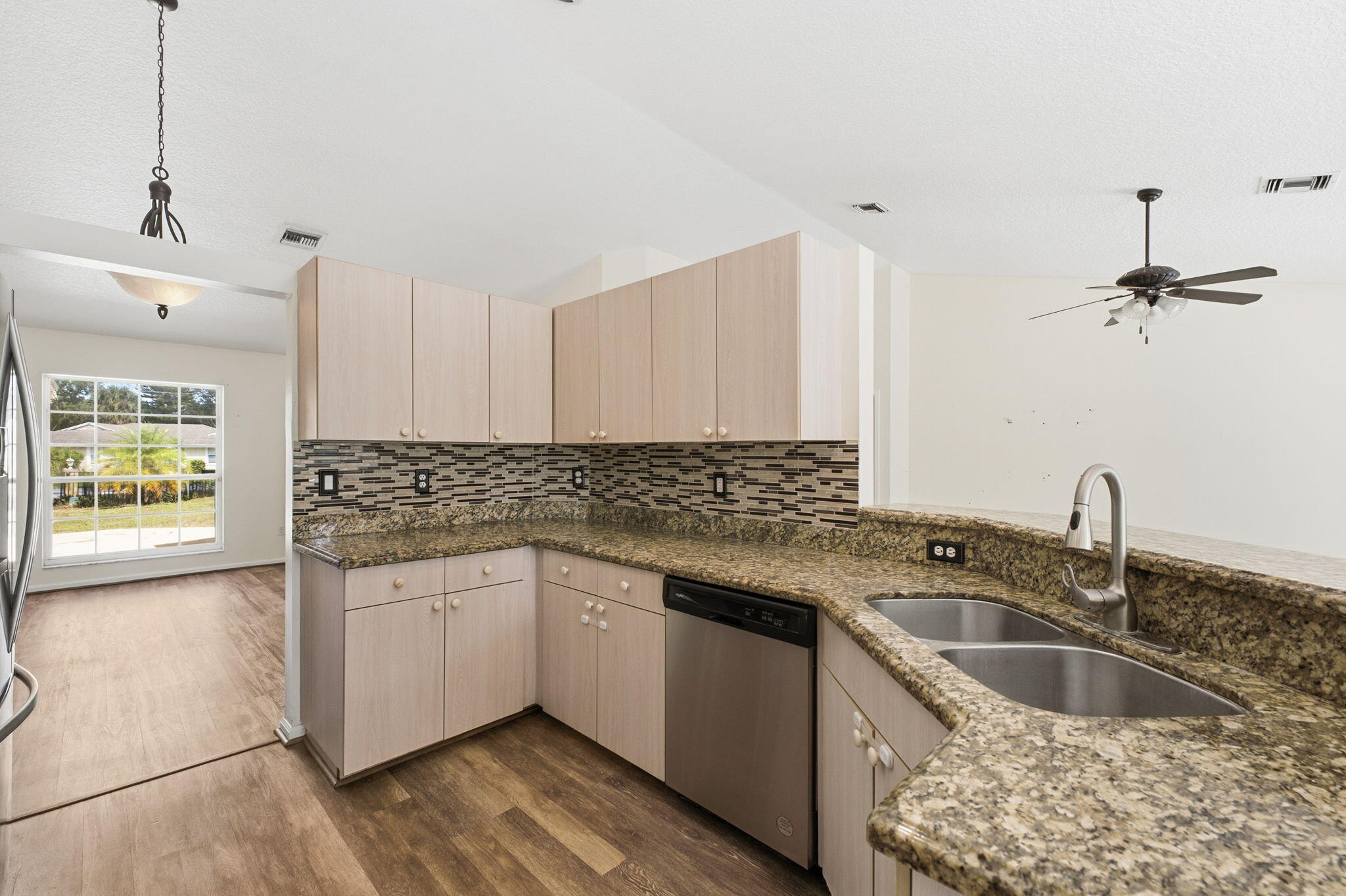 Kitchen featuring light-finish cabinetry, stone-surface countertops, decorative stone-tile backsplash, stainless steel dishwasher, and dual-basin undermount sink with a high-arc pull-down faucet