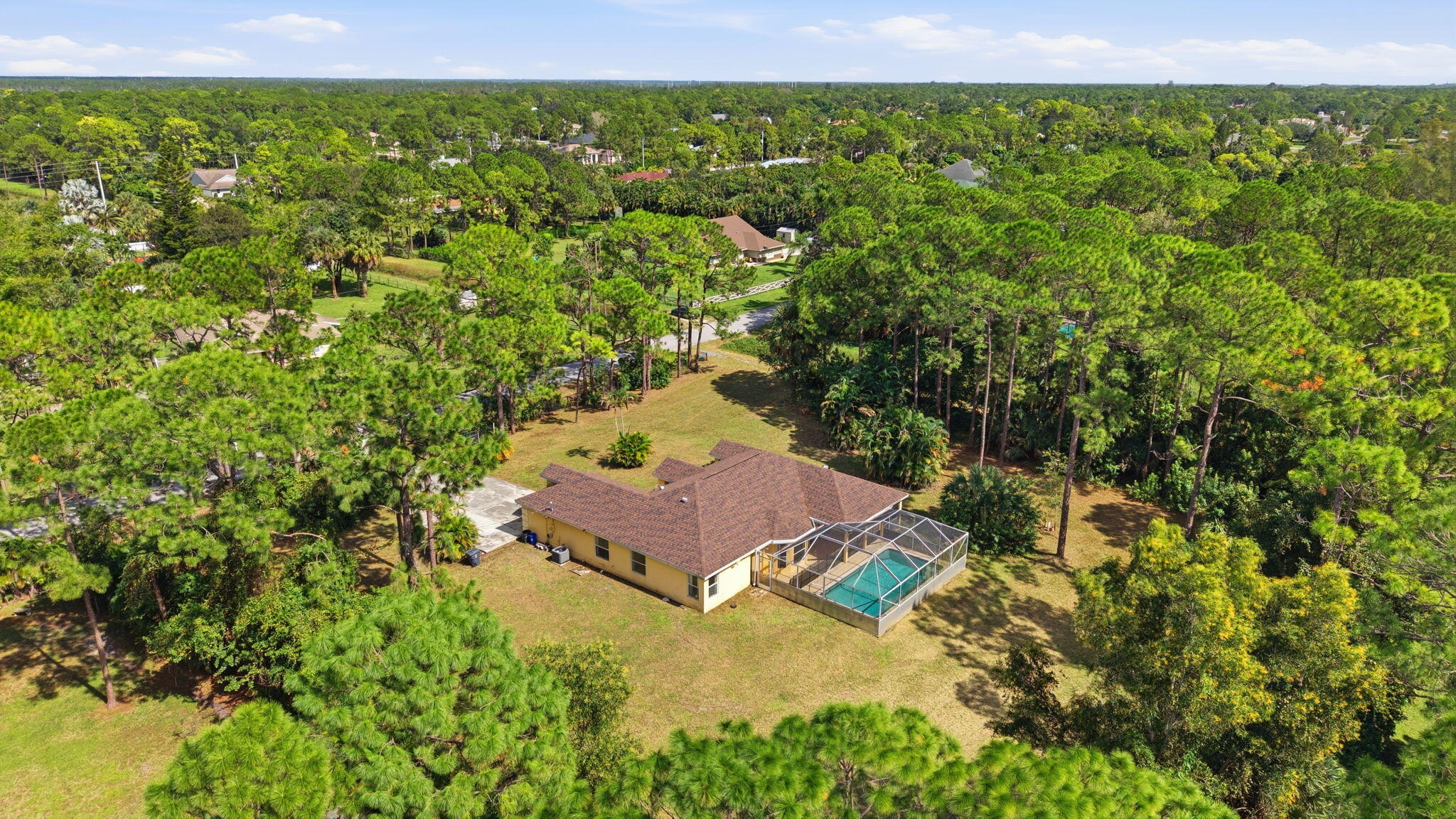 Aerial view of a sprawling property featuring a multi-gabled roofline, an enclosed pool, and extensive grounds surrounded by mature trees