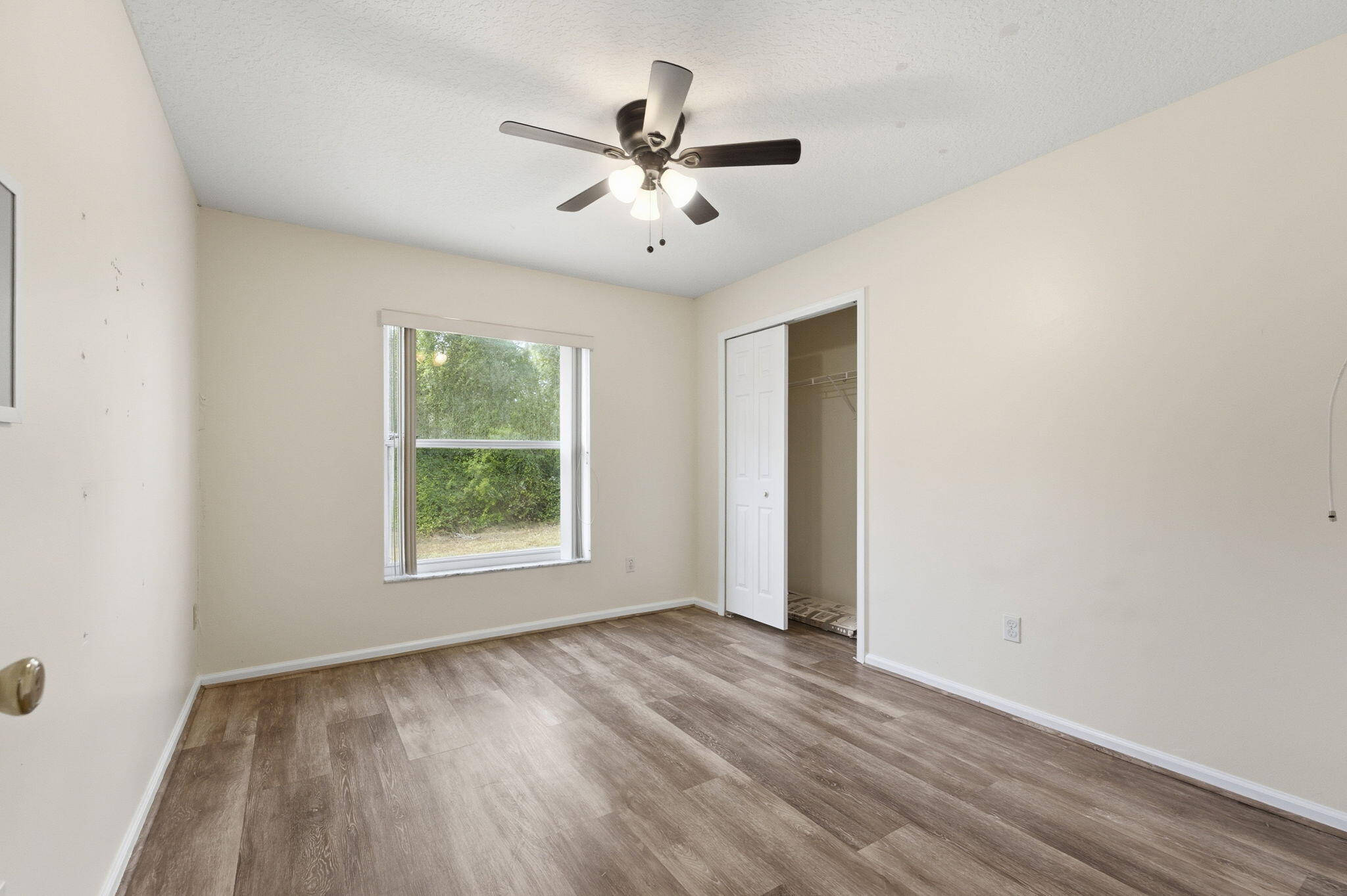 Wood-finish flooring, ceiling fan with integrated lighting, window with horizontal blinds, and closet with sliding door