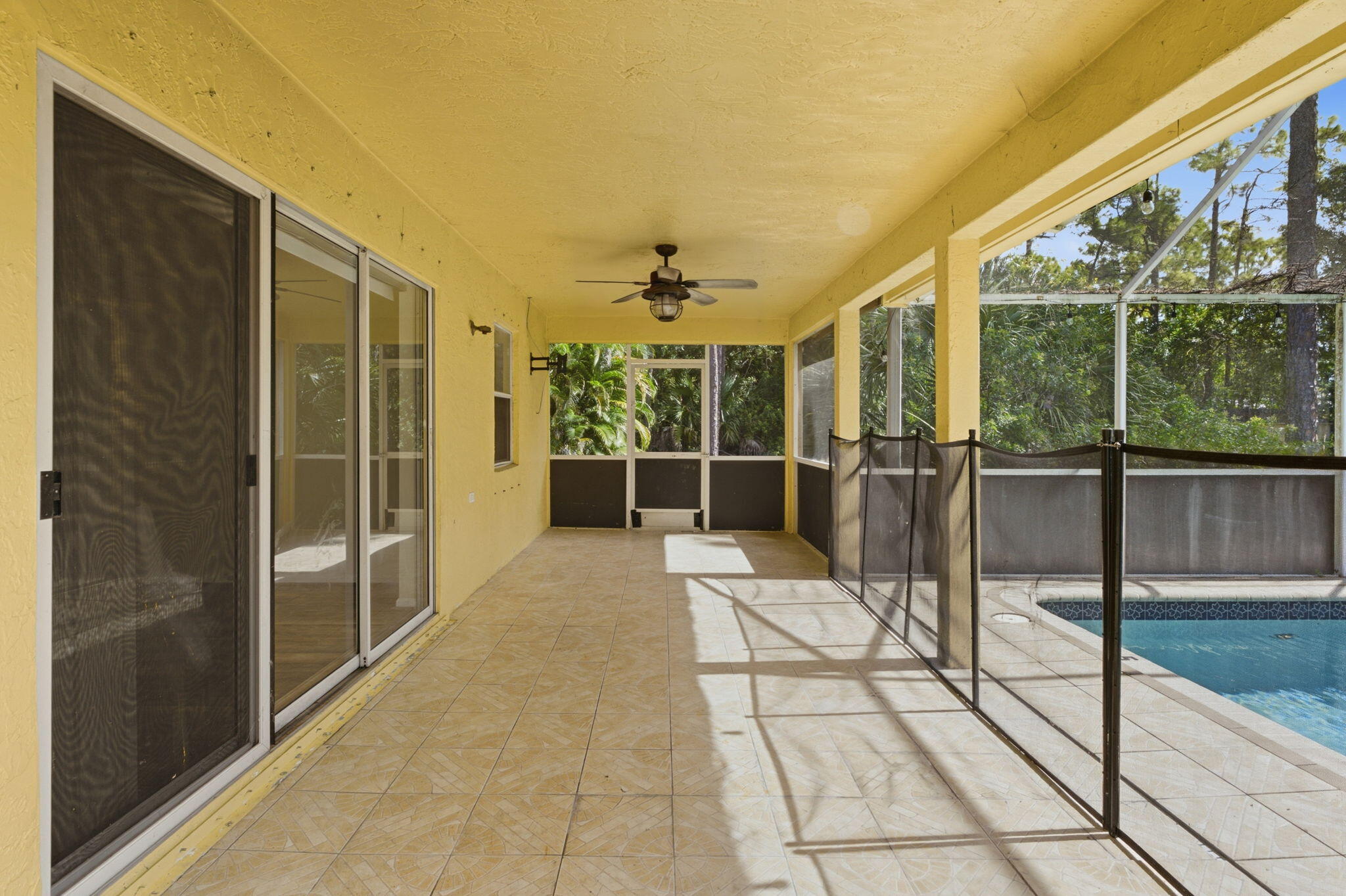 Covered lanai featuring tile flooring, ceiling-mounted fan, screened enclosure, and in-ground swimming pool