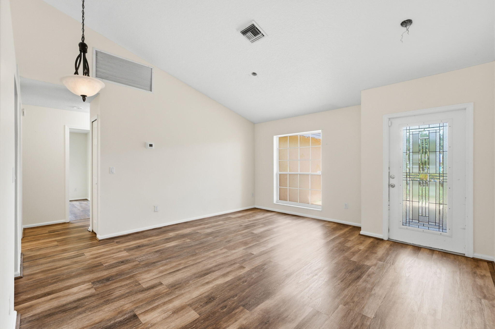 Vaulted ceilings, wood-finish flooring, an exterior door with decorative glass inlay, and a multi-tiered pendant light fixture